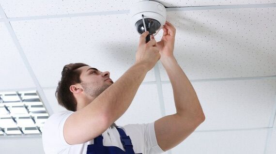 Electrician wearing safety gloves repairing a wall electrical outlet and switch box during home electrical maintenance.