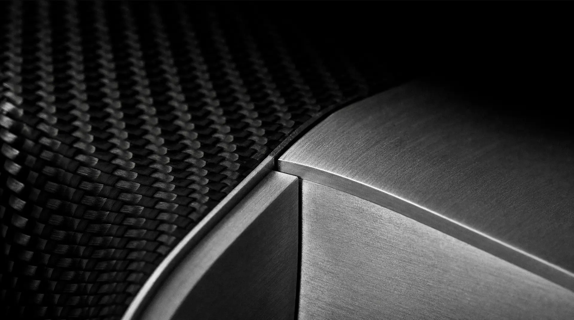Macro view of carbon-fiber weave beside a brushed metal panel edge, suggesting branding for tech companies.