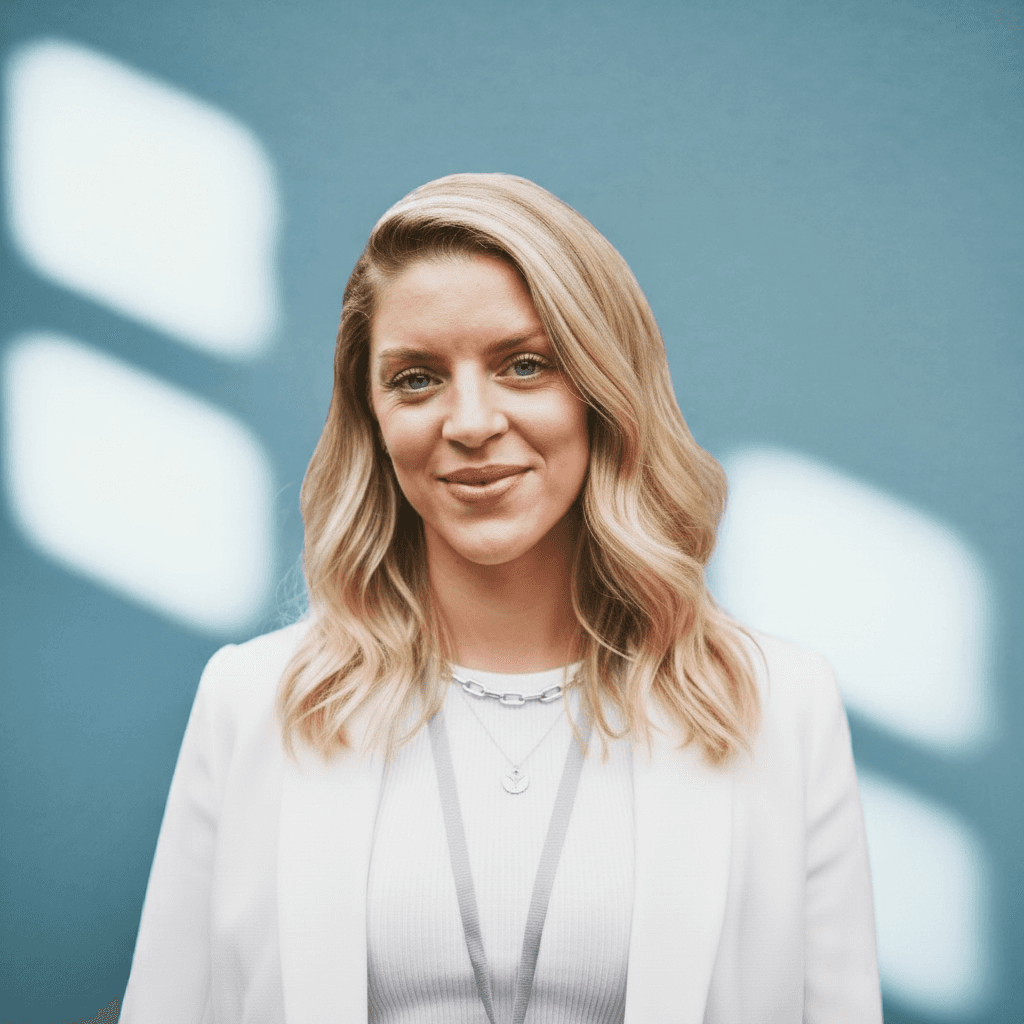 Portrait image of Samantha Davies, facing the camera and smiling. Background colours are soft and neutral, with sunlight reflected on the wall behind the subject.