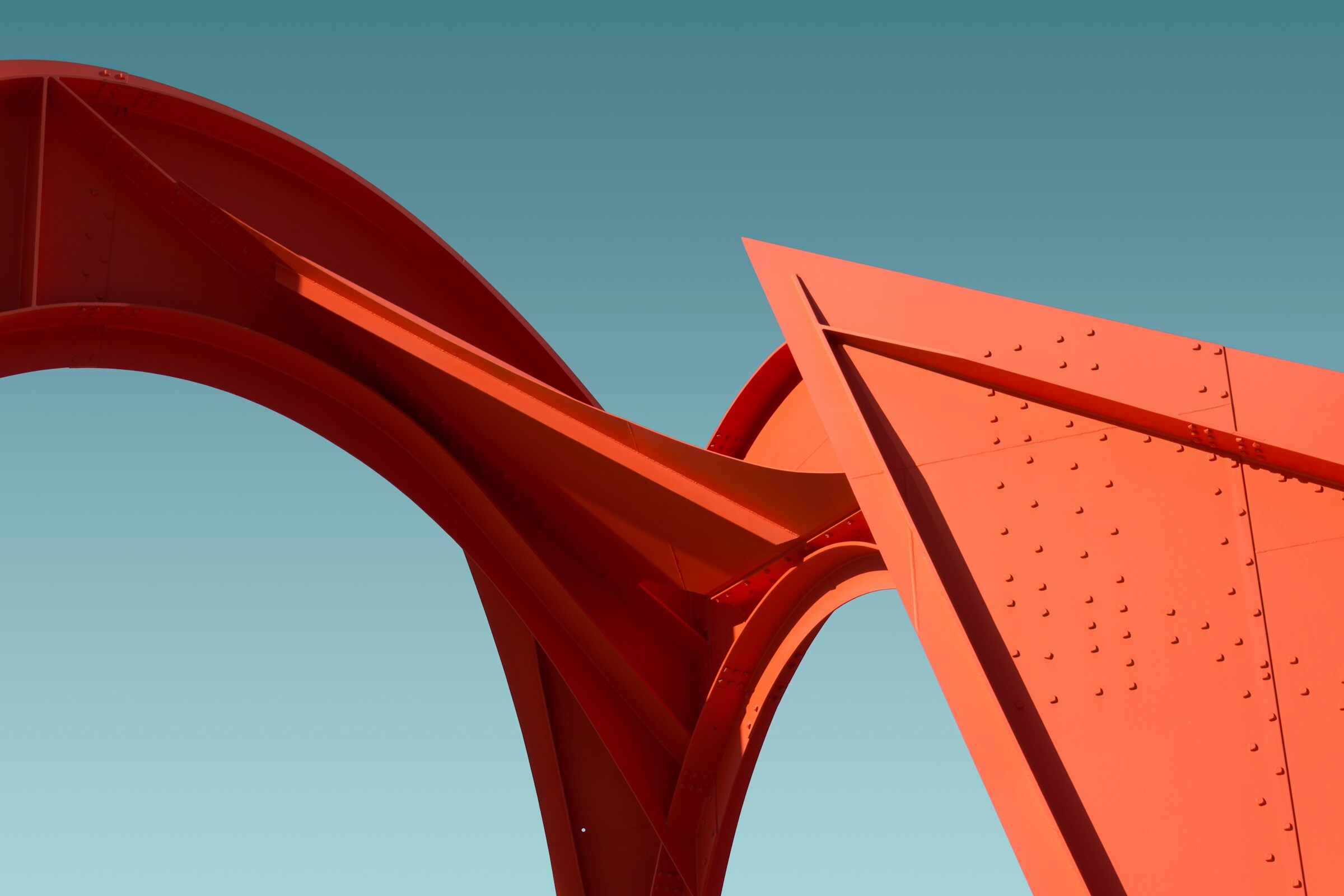 Minimalist close-up of a large red steel architectural sculpture against a clear blue sky.