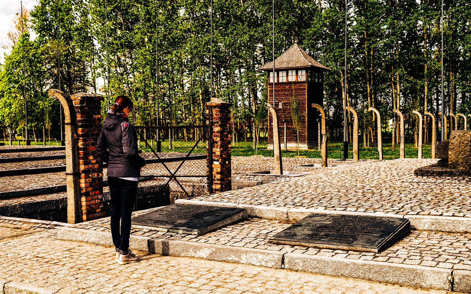 Besökare vid Auschwitz-Birkenau minnesplats med vakttorn i bakgrunden, Polen.