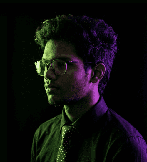 Designer Divakar V wearing a formal shirt and tie, looking off-camera in dramatic lighting.