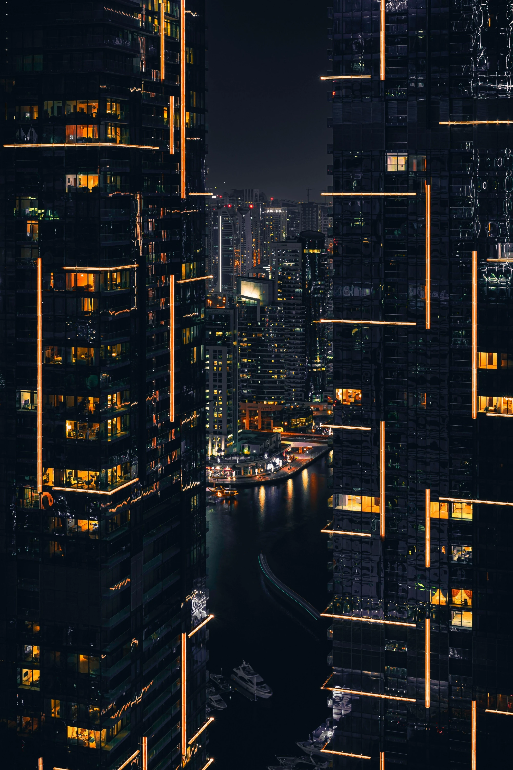 Nighttime cityscape with towering skyscrapers adorned with vertical orange lights, framing a river and marina, conveying modernity and bustling urban life.