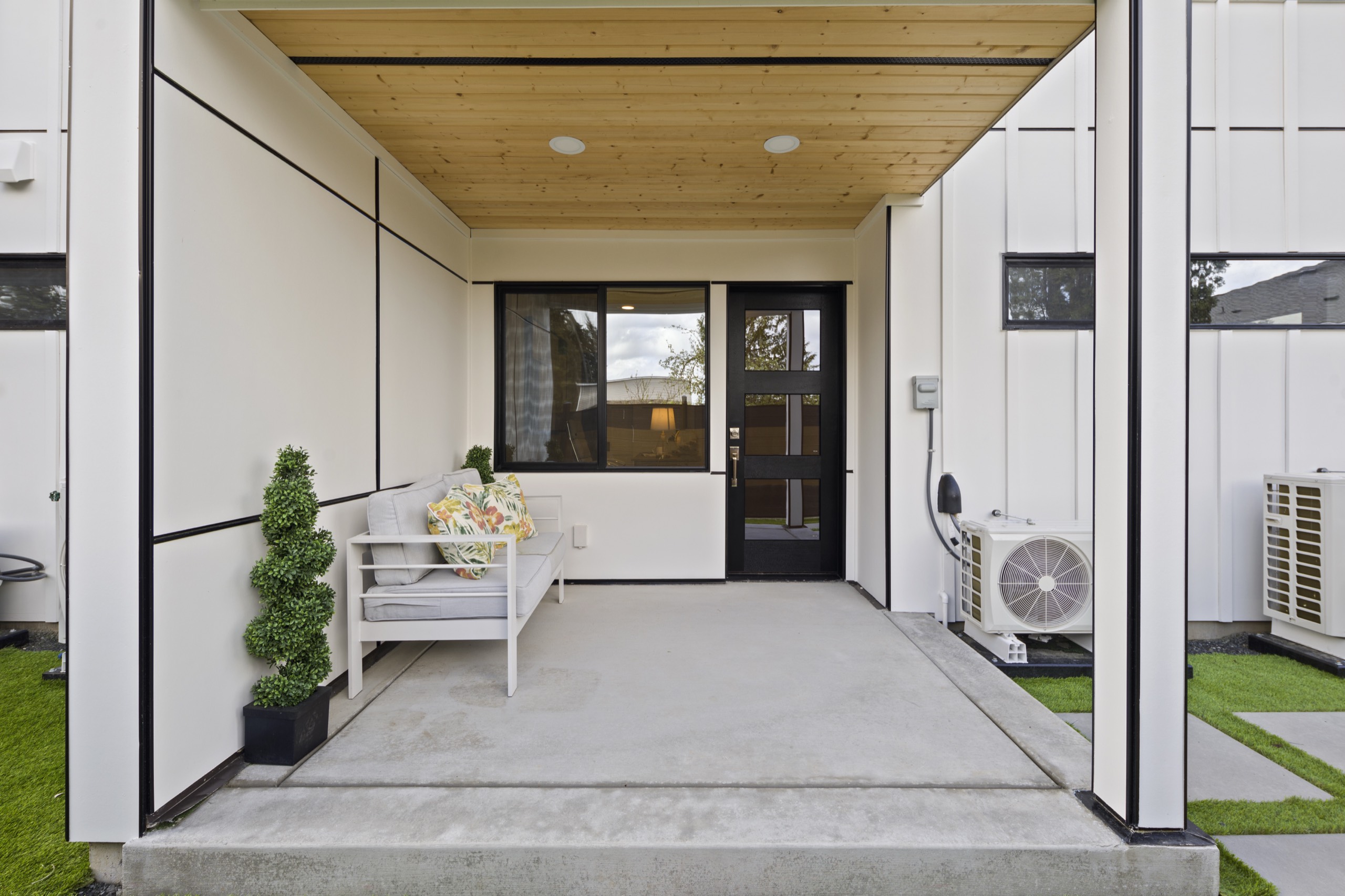 Covered ground-floor patio of a luxury townhome with concrete flooring, white bench seating, black-framed glass door, cedar ceiling, and mini-split HVAC unit