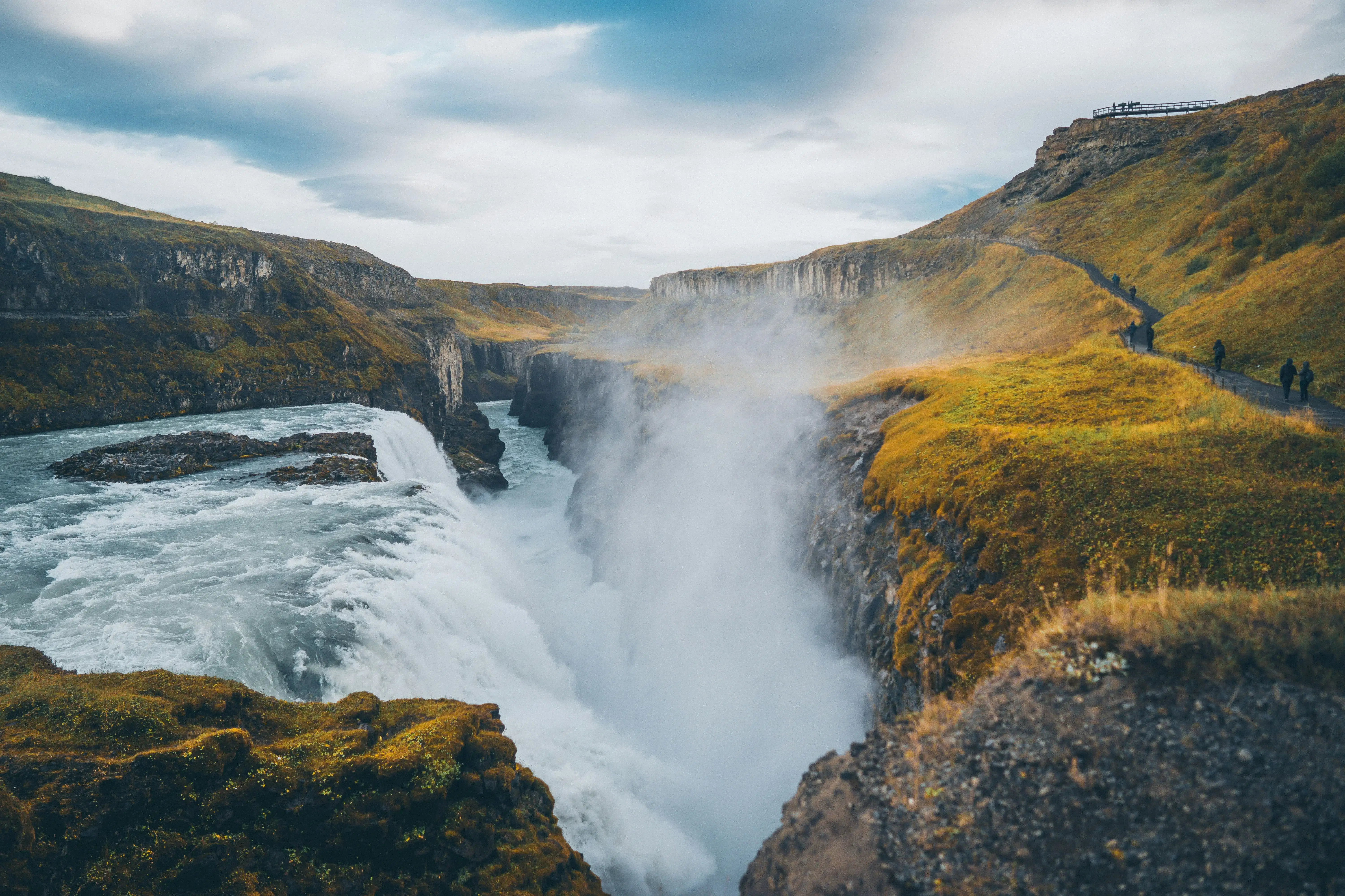 Large waterfall cascading into a deep canyon surrounded by green cliffs under a cloudy sky.