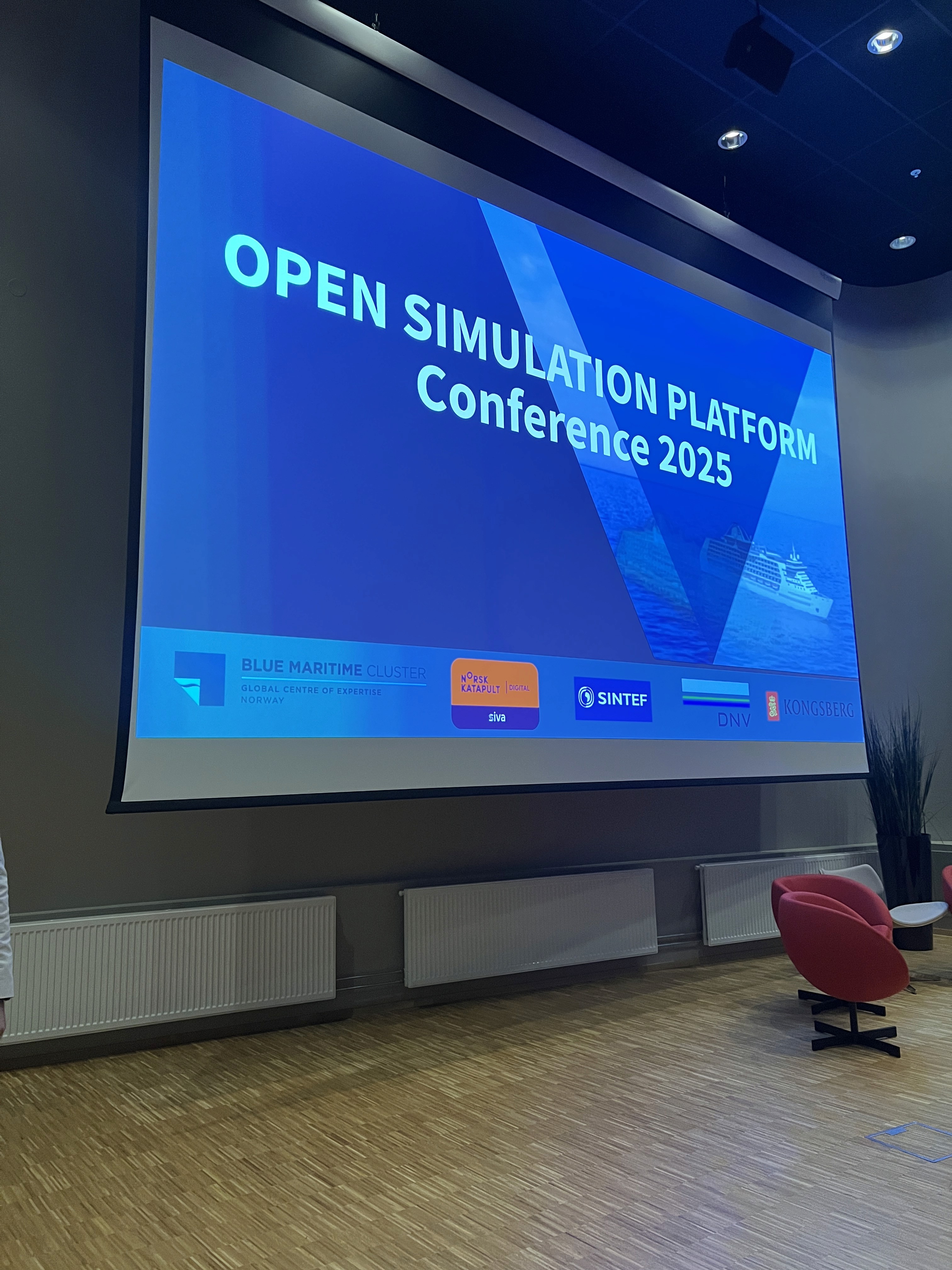 Presentation screen displaying "OPEN SIMULATION Conference 2023" in a conference room setting.