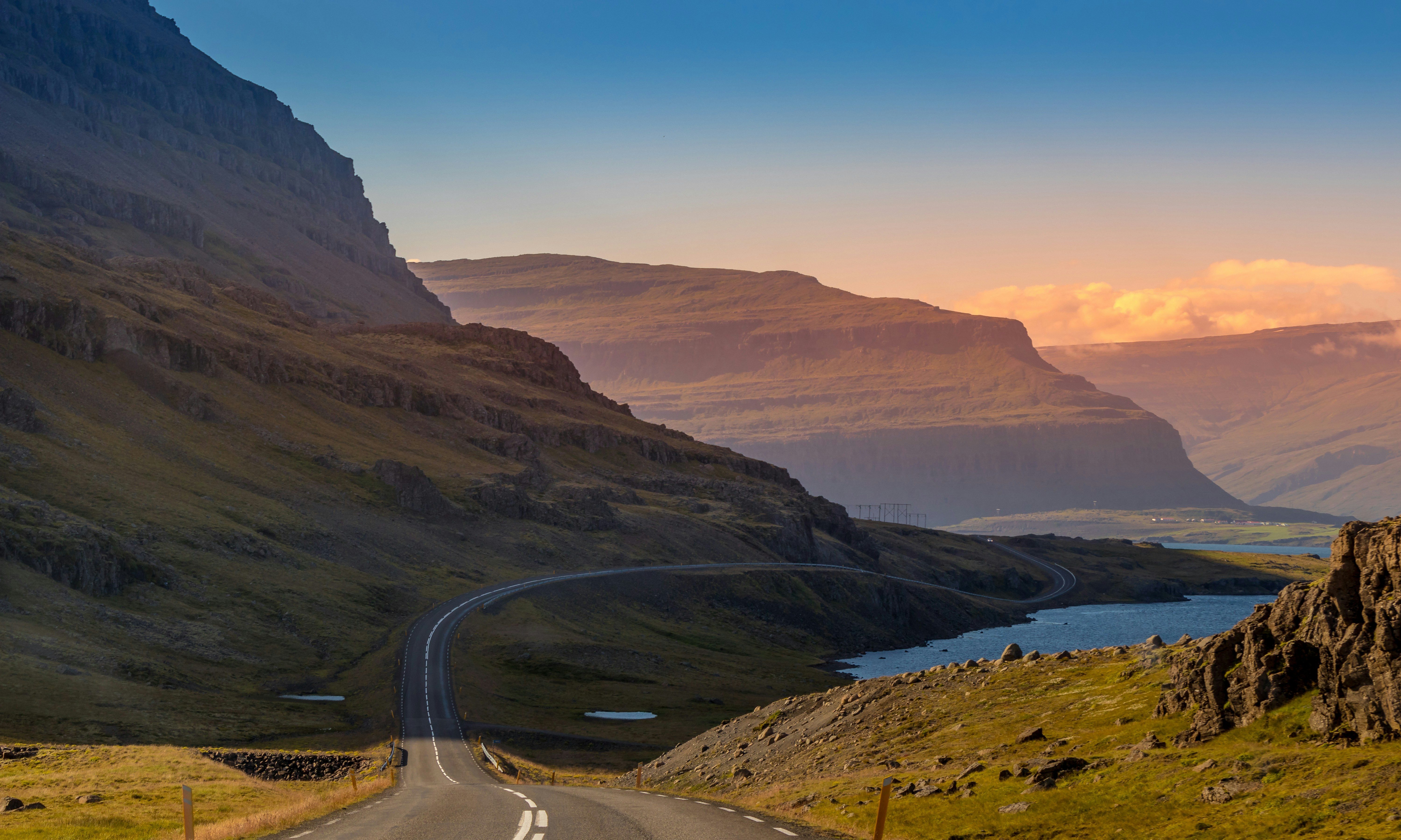 Scenic road winding between Icelandic mountains beneath pink skies.