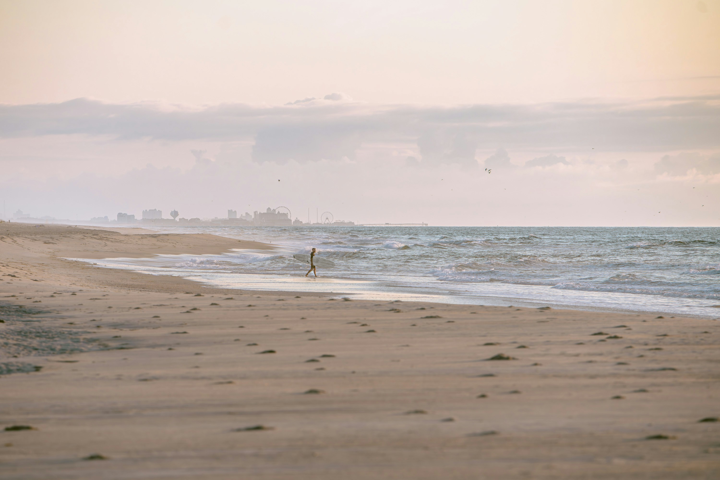 A lone figure walks on a sandy beach near the ocean.