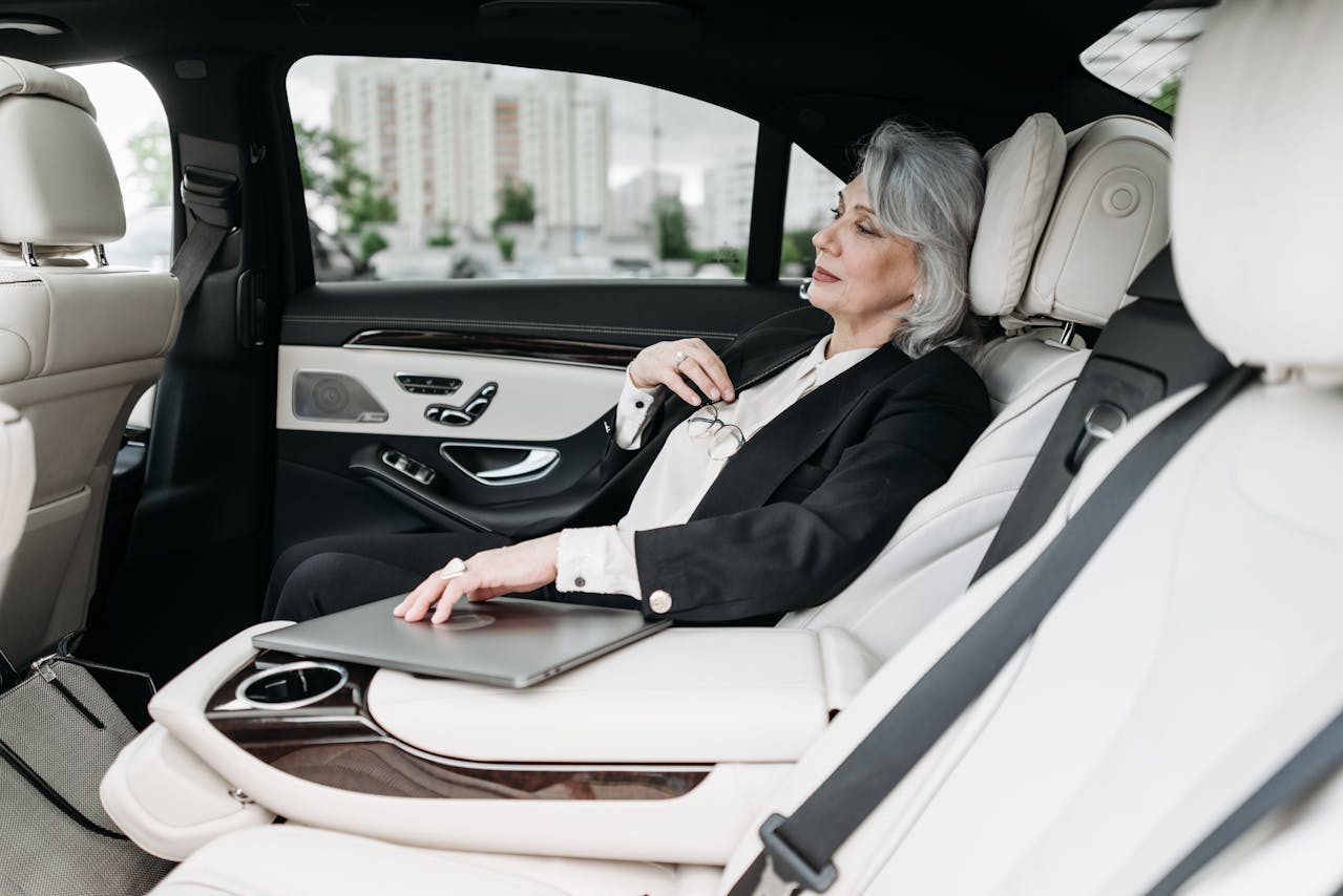 Luxury chauffeur service passenger in high-end vehicle, relaxed in plush leather seat, laptop on armrest, exuding elegance and comfort during transportation.