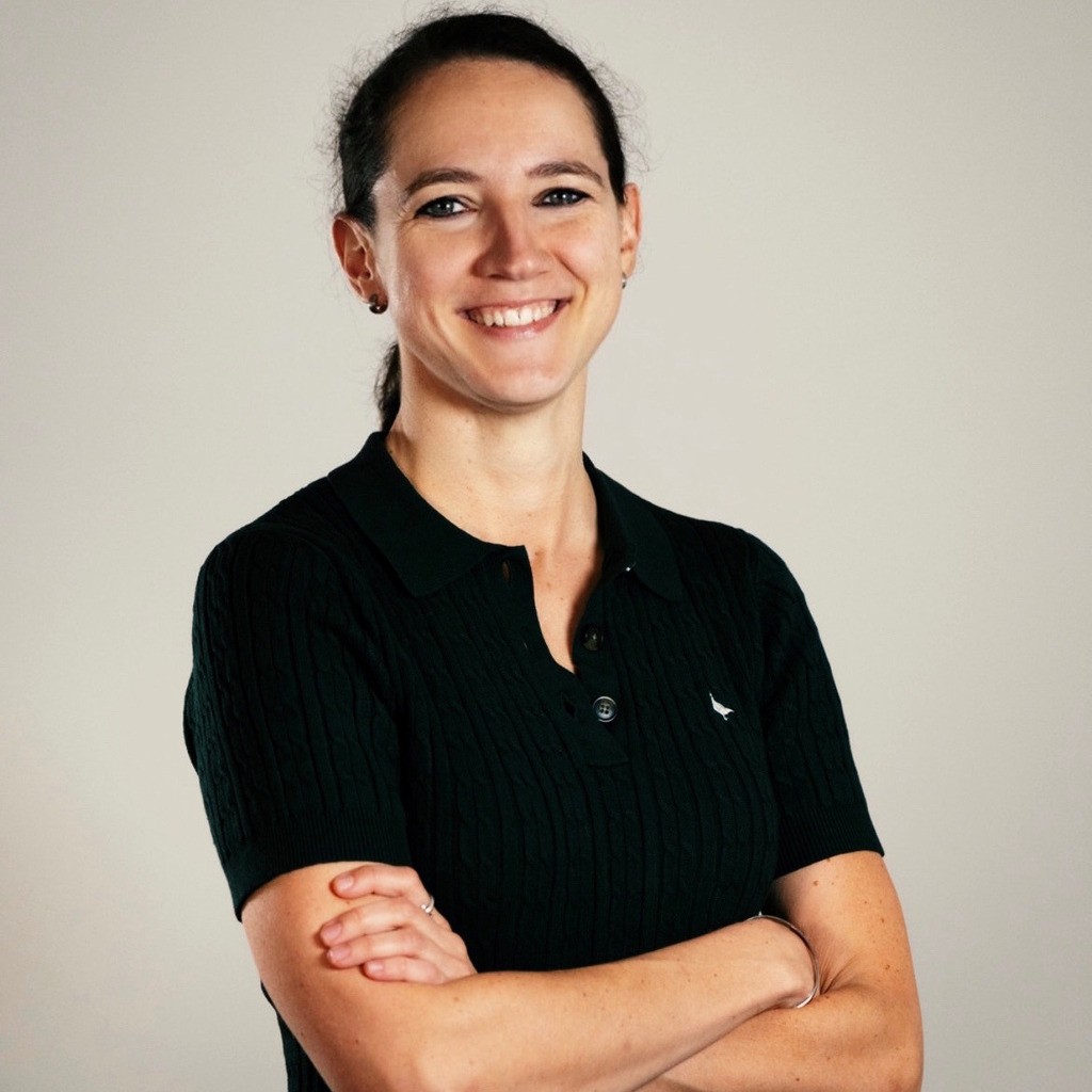 Foto von Sanela Thunig mit einem schwarzen Poloshirt vor einer beigen Wand