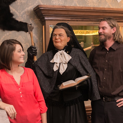 两个人站在穿着历史服装的蜡像旁边，手里拿着一本书。他们都在一个类似博物馆的环境中。