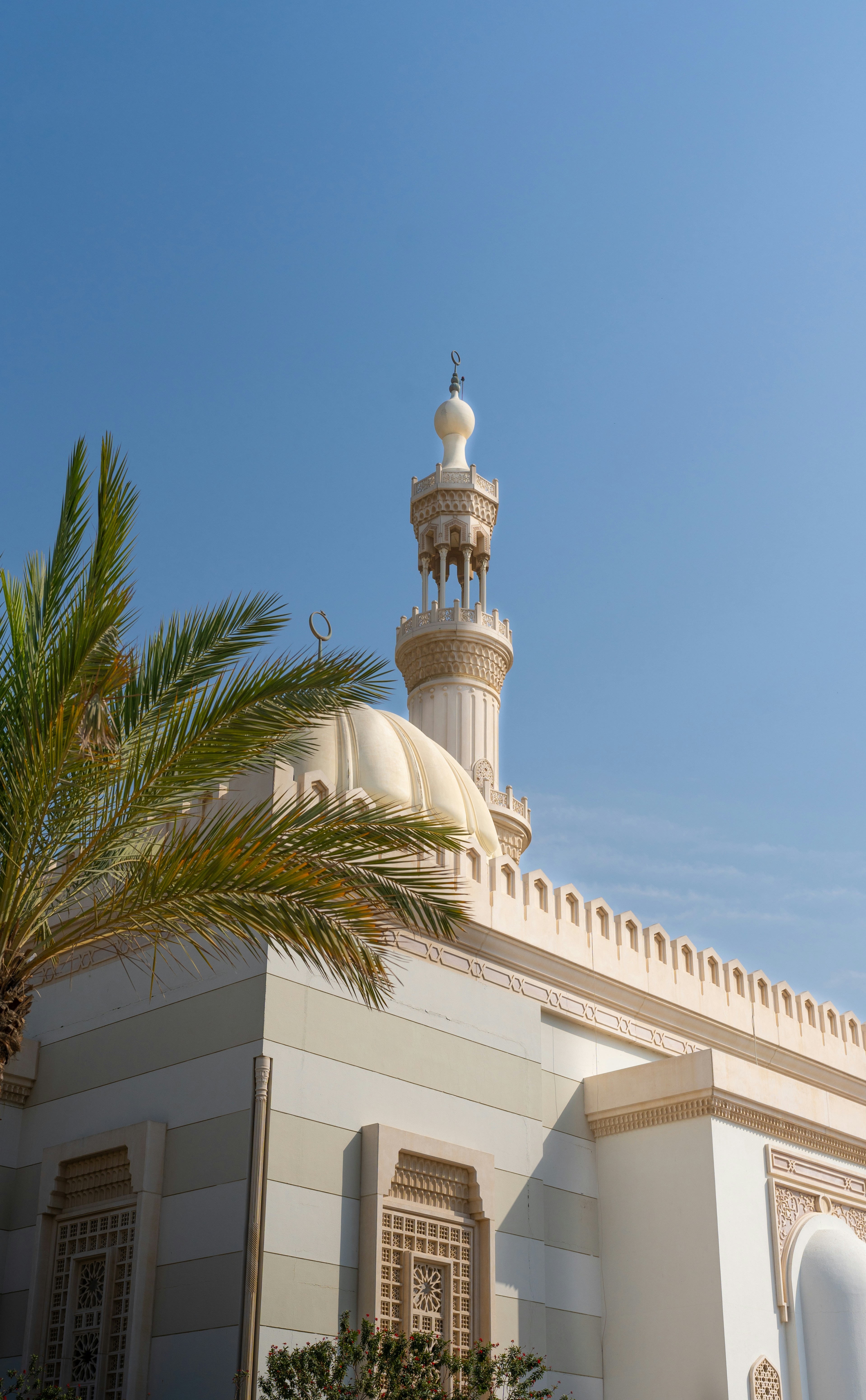 Exterior view of a white stone mosque with a traditional minaret and dome against a clear blue sky.