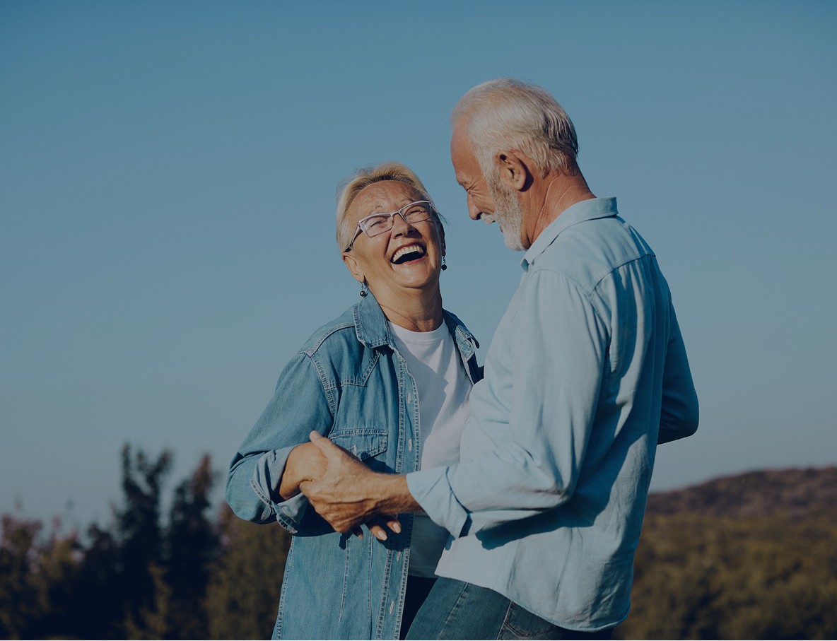 Two older people laughing together against a blue sky