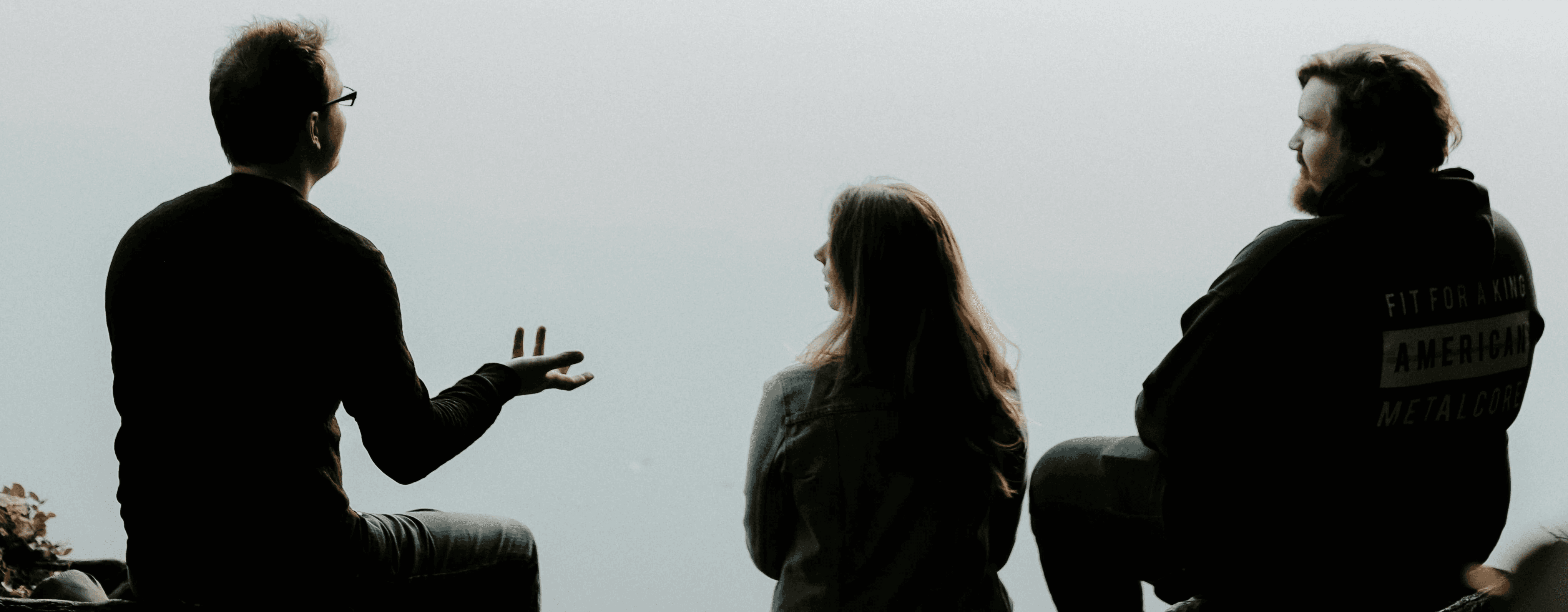 silhouette of three people sitting on cliff under foggy weather
