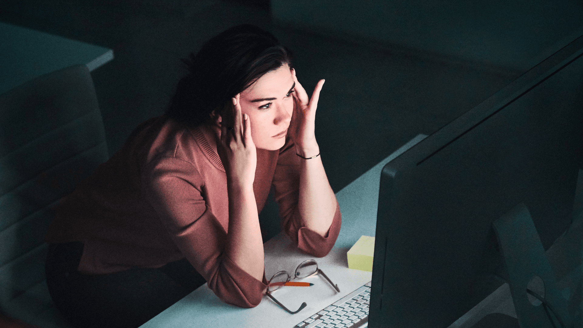 A winding road cuts through rocky terrain, surrounded by patches of green grass and illuminated by sunlight.