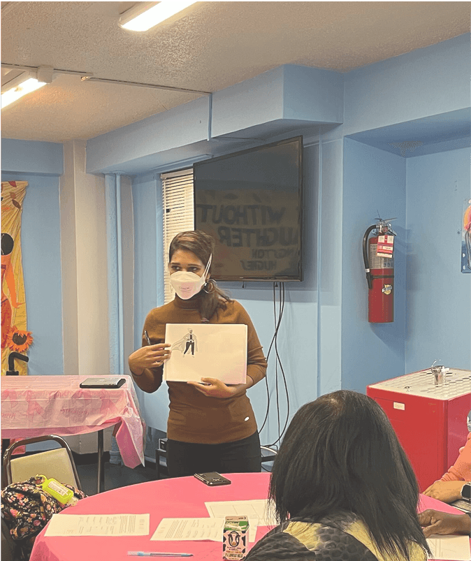 Tanu, an indian woman with a mask, holds up a piece of paper in front of older people in a senior center.