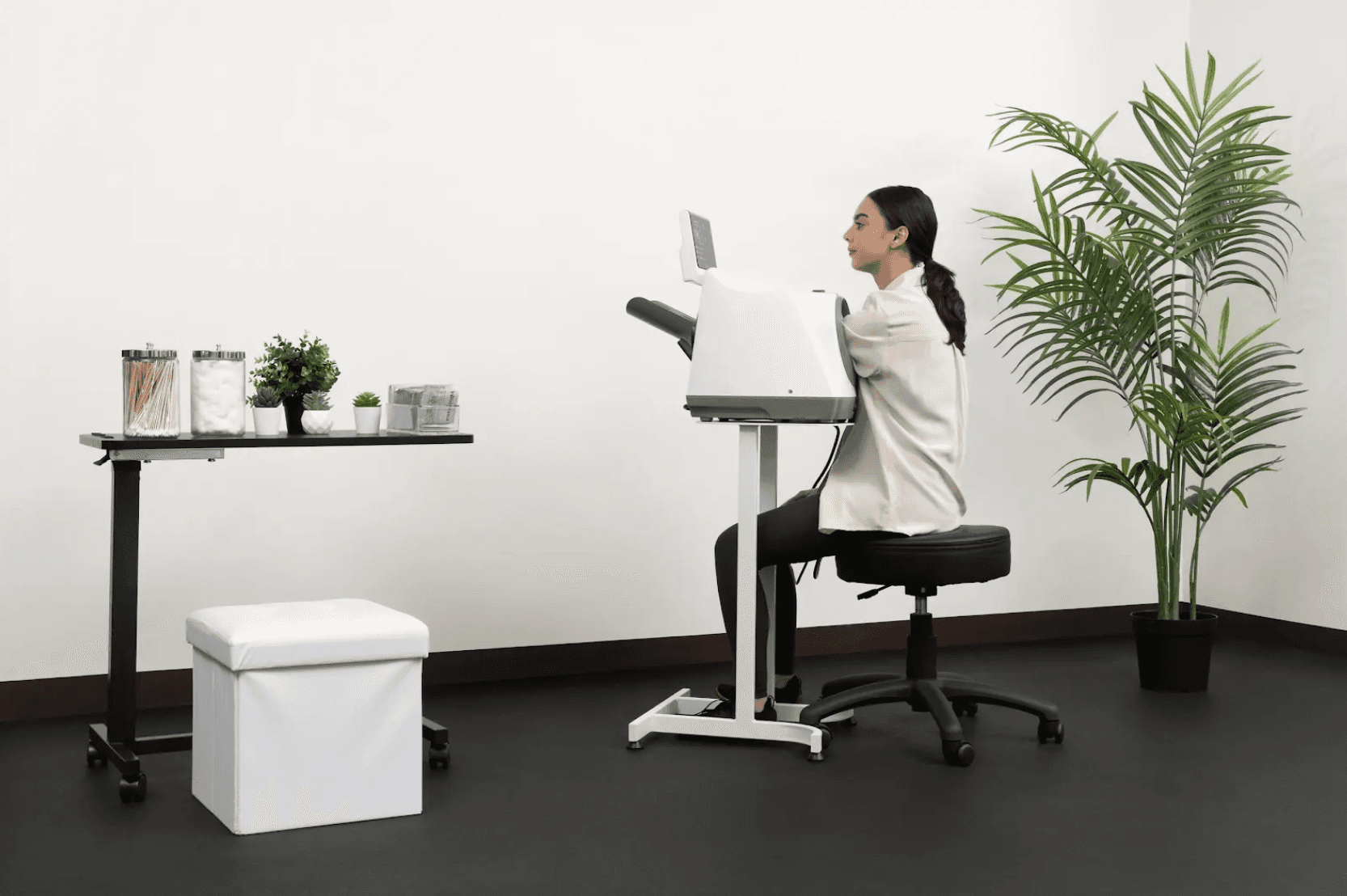 A woman sitting on a stool using an InBody BPBIO professional automatic blood pressure monitor on a mobile stand in a modern clinical setting.