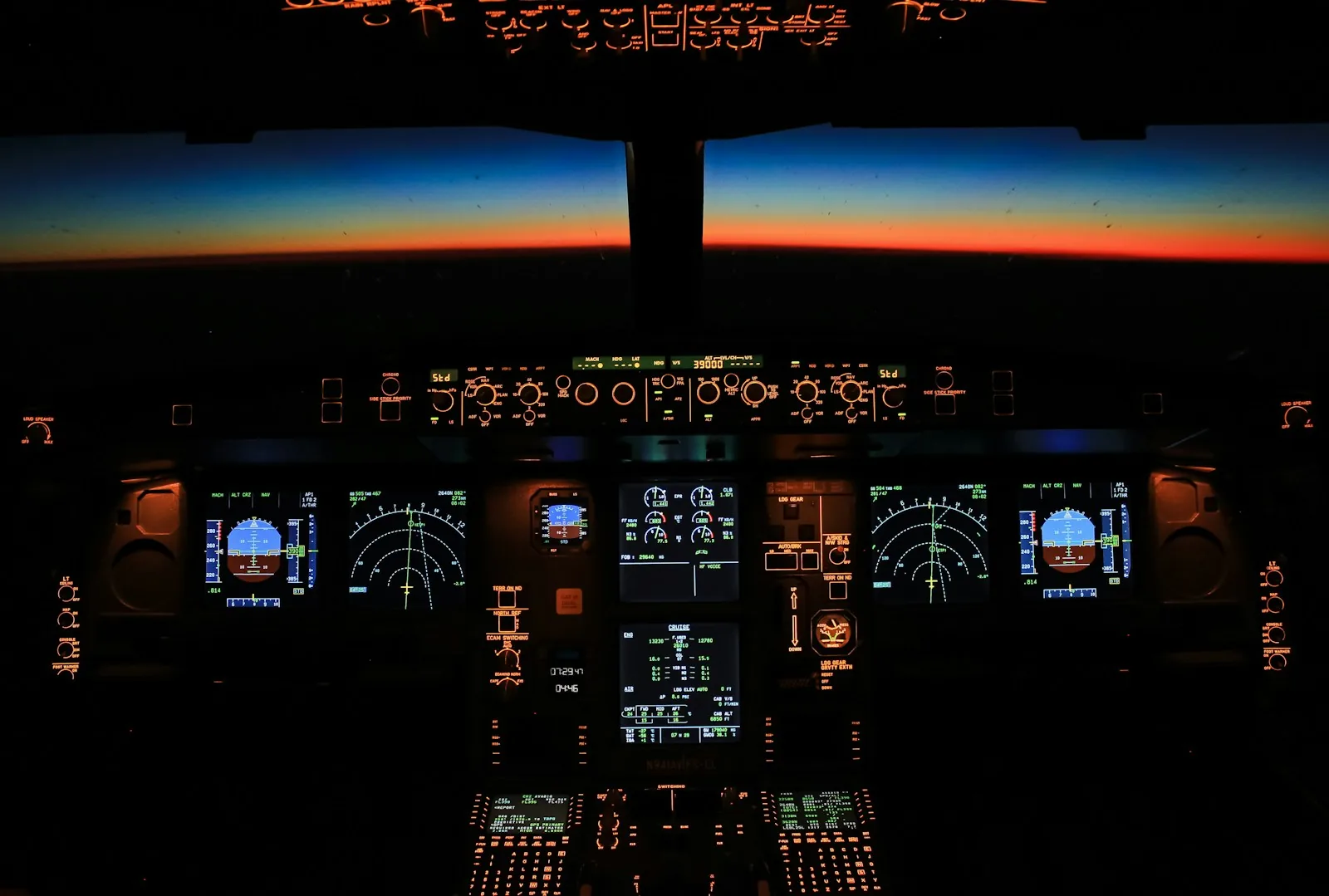 Airliner cockpit instrument panels glowing at dusk with the horizon visible through the windscreen