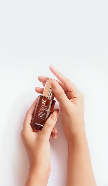 Hands holding an amber glass serum bottle against a white background