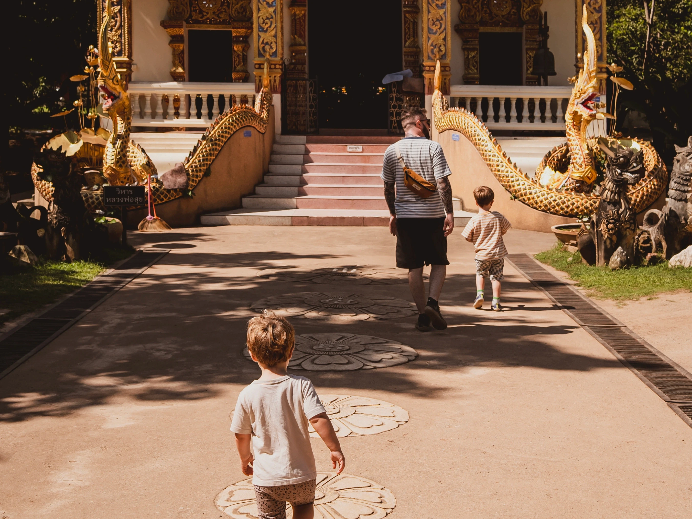 A father and two children walking toward an ornate temple entrance flanked by golden dragon statues.