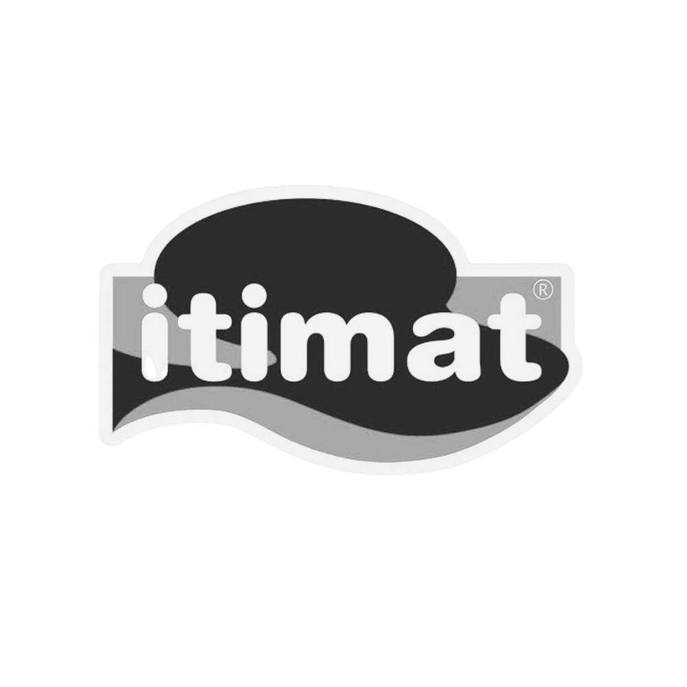 A woman with blonde bob hair in a grey coat and beige turtleneck stands against a neutral backdrop. She has a serious expression, conveying elegance.