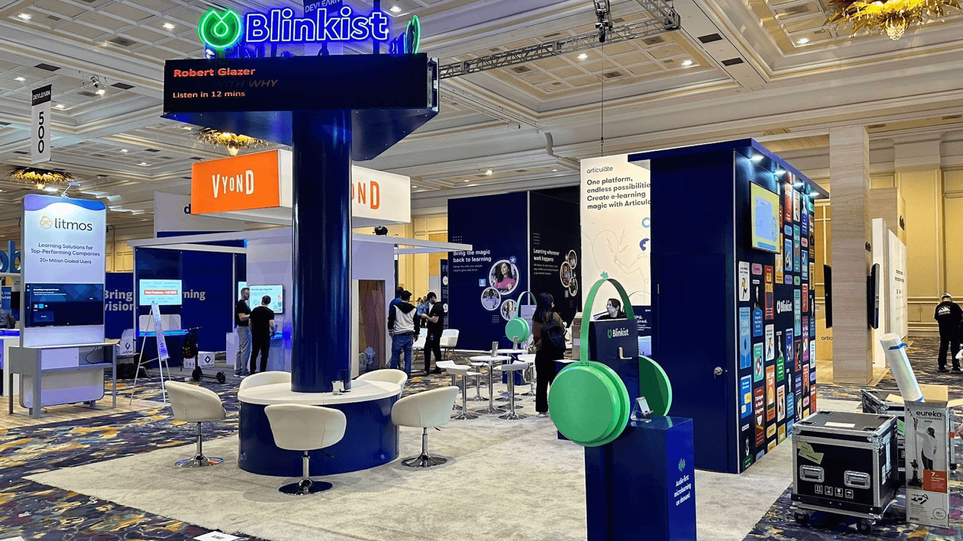 Blinkist DevLearn Conference & Expo 2025 20x40 technology product demo booth with illuminated tower sign, seating ring, headphones display stand, and side graphic wall