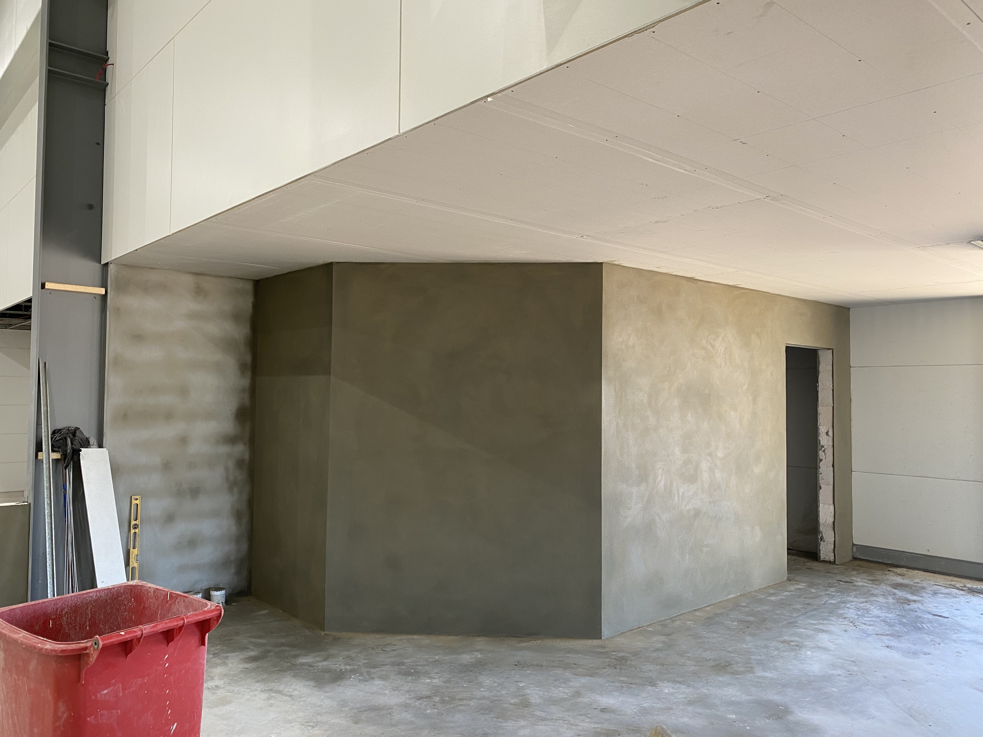 A modern hallway features vibrant teal and orange geometric and leaf patterns, with glossy tiled floors, a large rectangular light fixture, and a small shelf holding a potted plant, all leading to a large, frosted window at the end.
