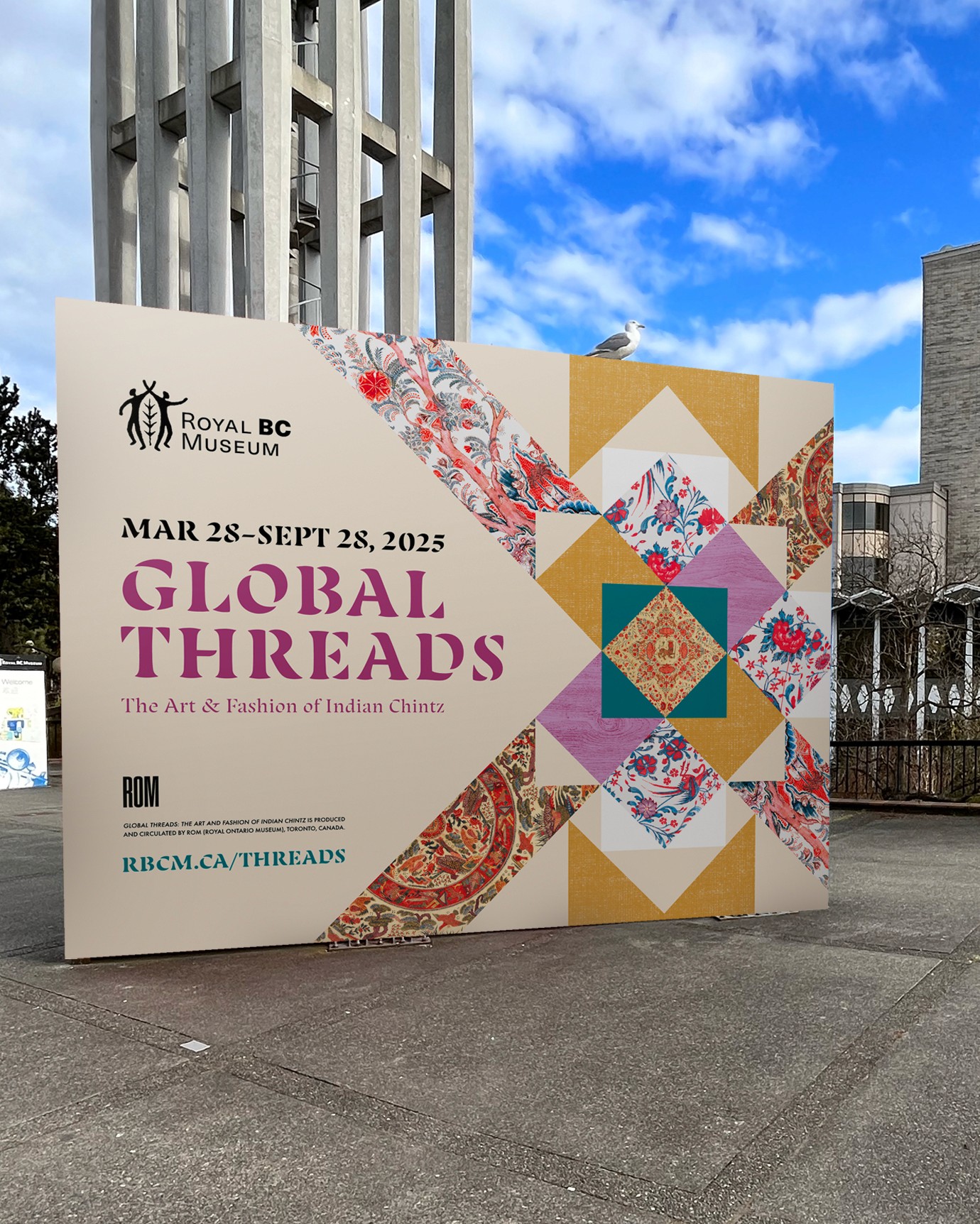 A horizontal street-level billbaord advertising an exhibition titled Global Threads