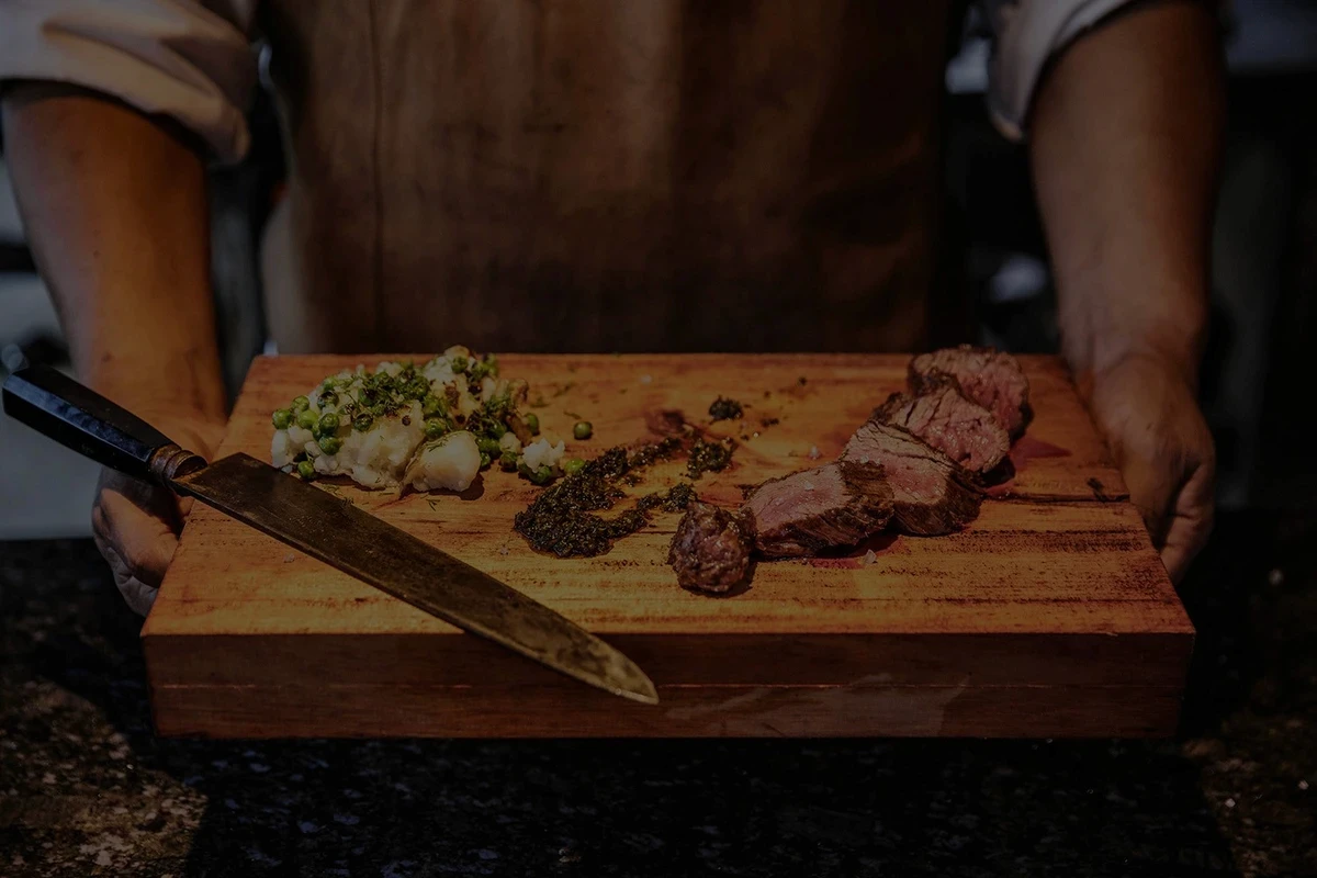 Restaurante 4 Fuegos en Be Tulum: carnes picadas sazonadas en una tabla de cortar sostenida por manos masculinas con un cuchillo.