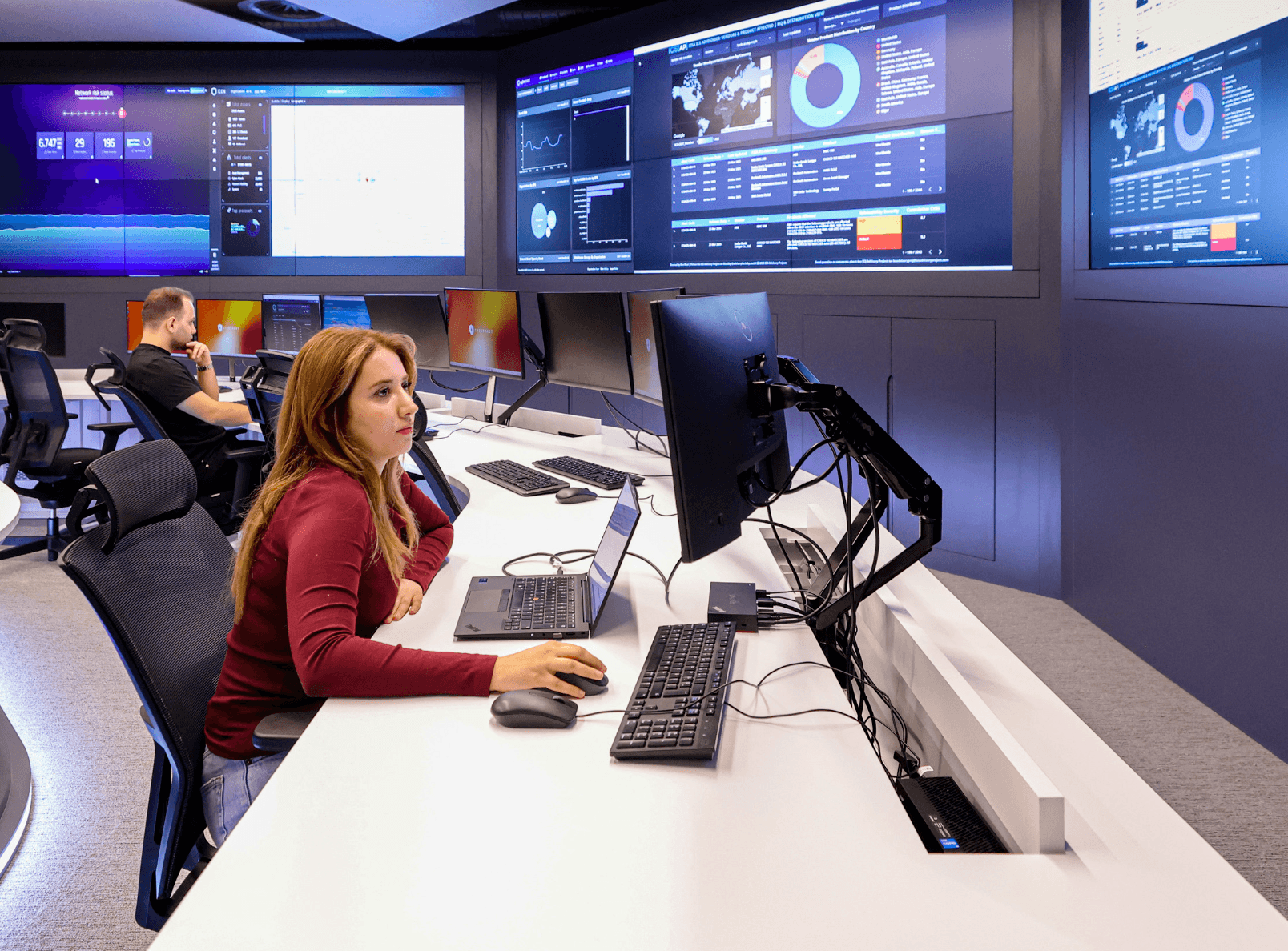 A person working at a computer in a modern office with multiple digital screens displaying data and graphics.