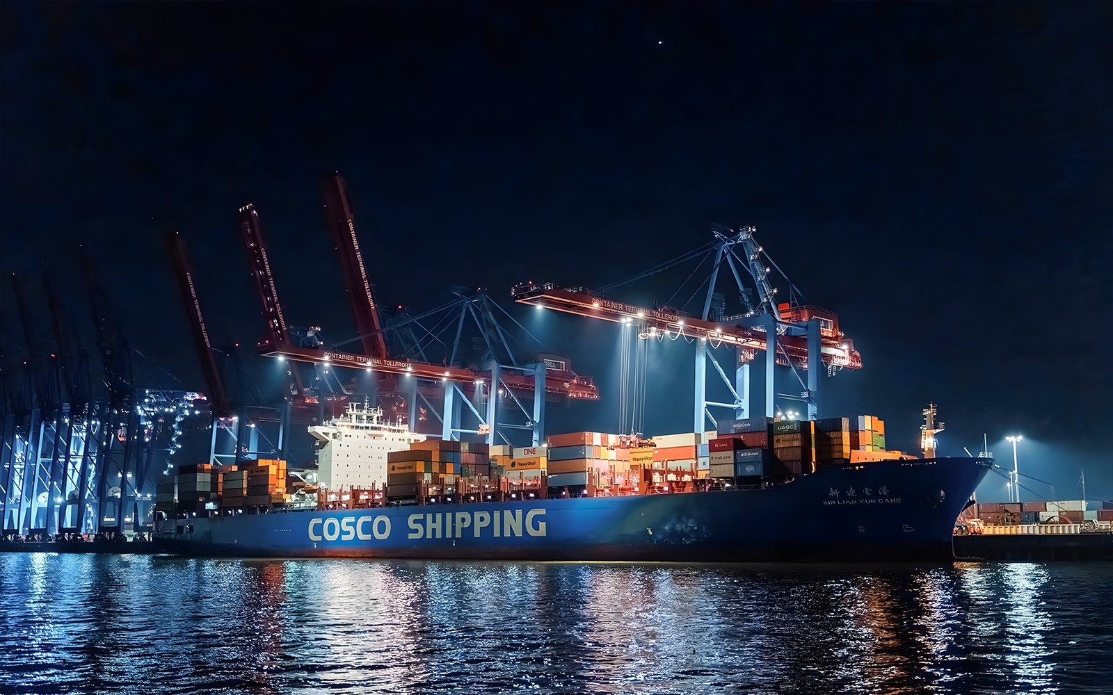 Large ship docked at night with illuminated cranes, part of the 1.5h Grand Evening Lights Cruise.