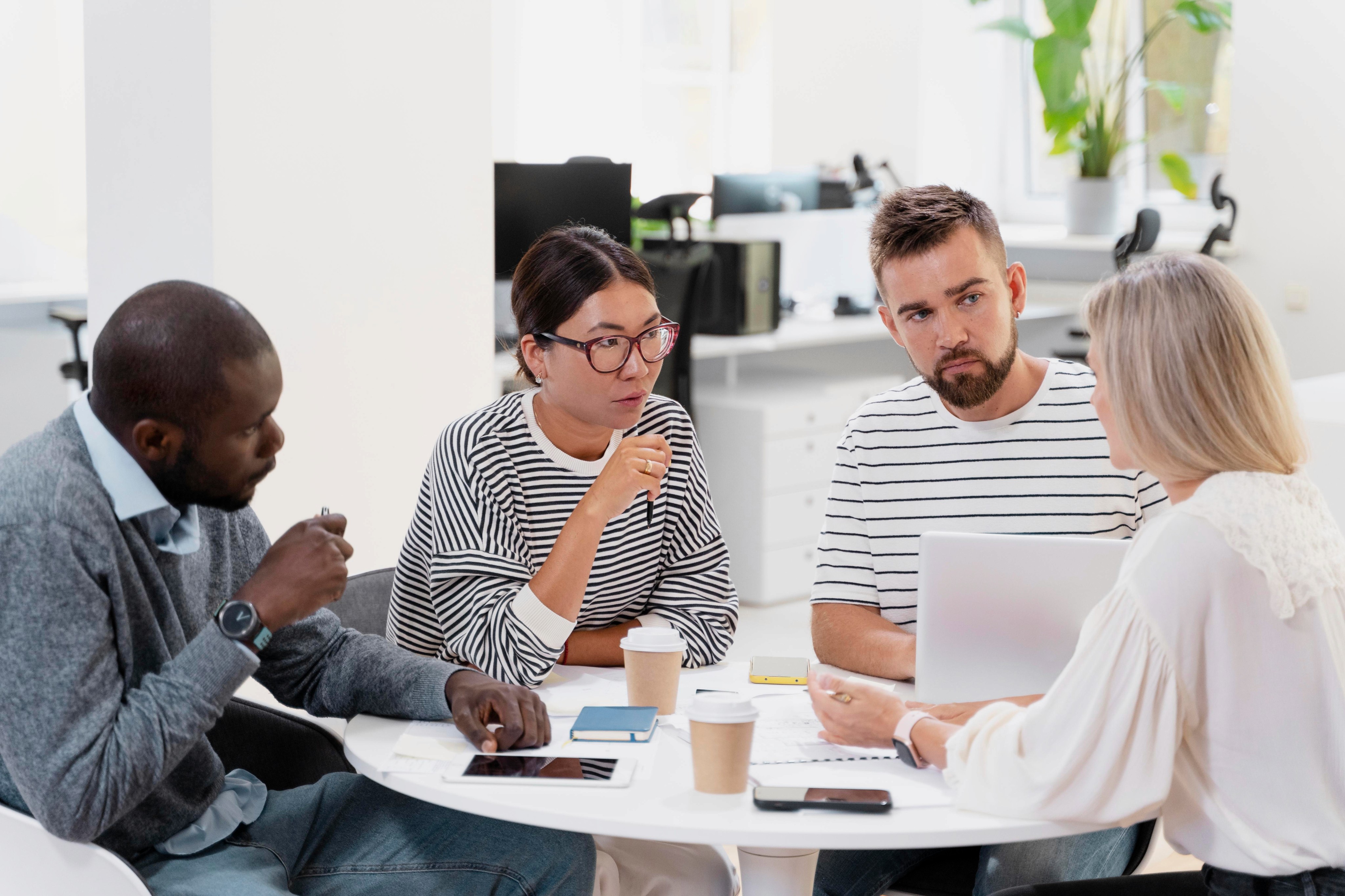 Four colleagues discussing around a table with a laptop.