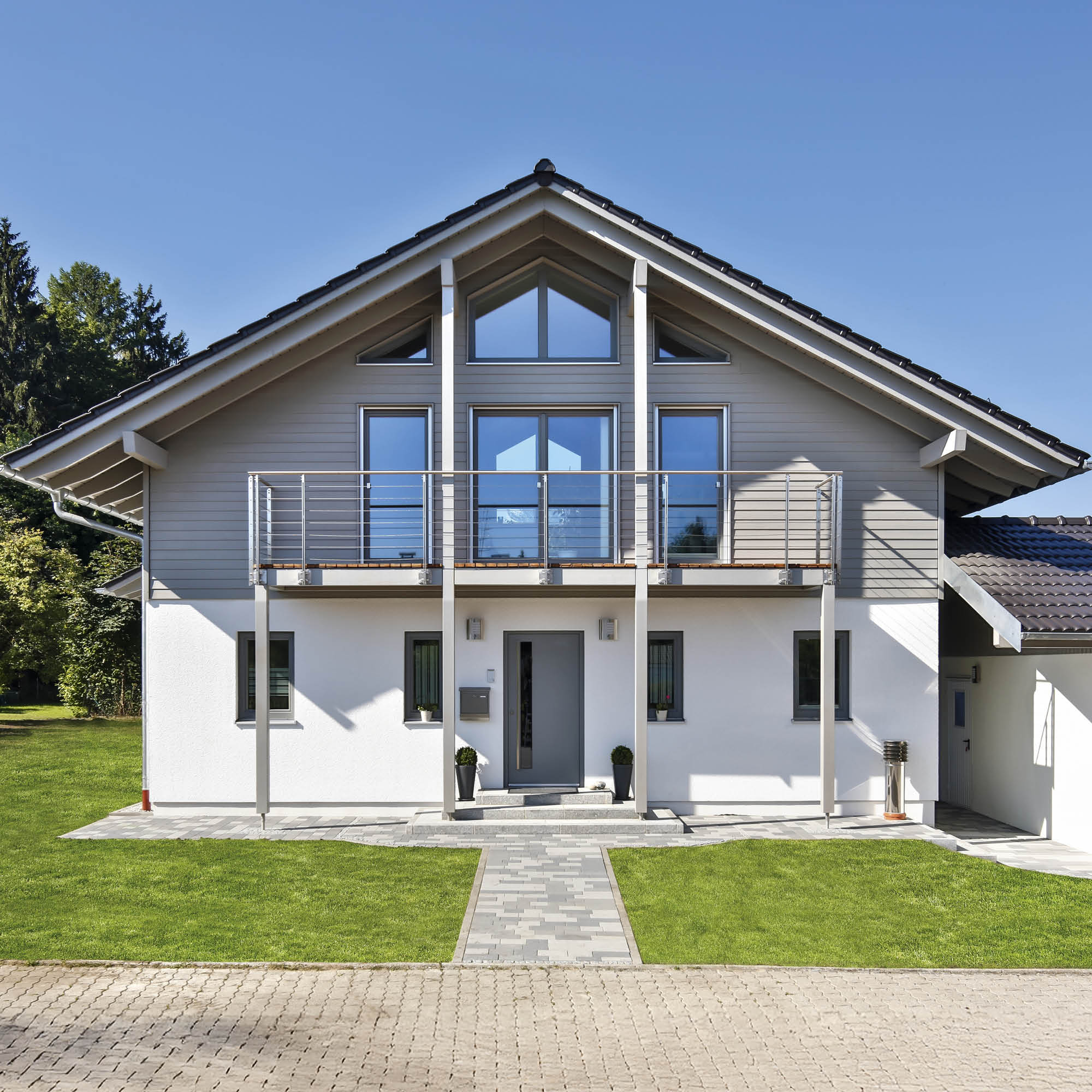 Moderne weiße und graue Fassade mit großen Fenstern, Balkon und gepflegtem Garten.