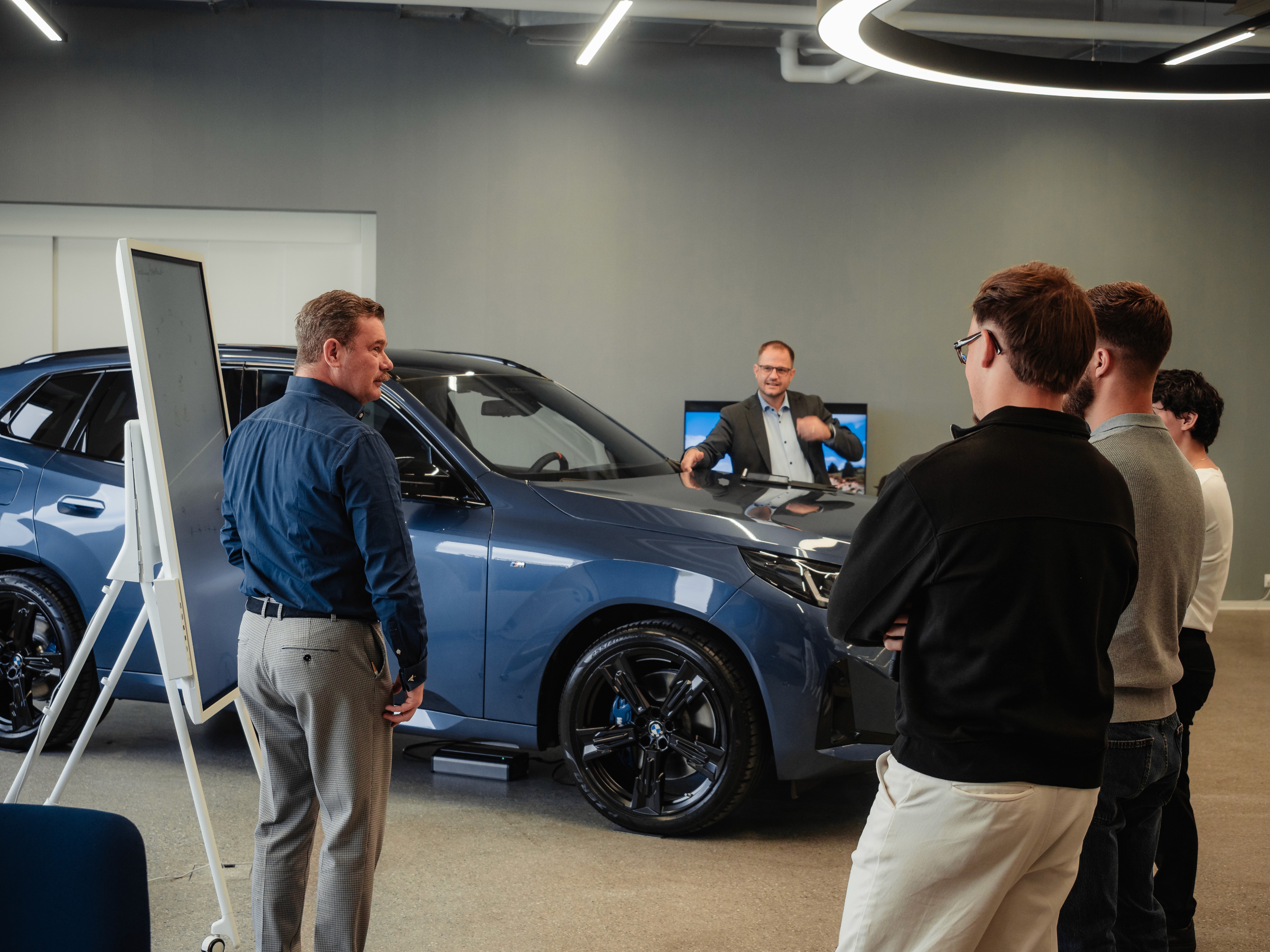 Trainer guiding a group through automotive product training, explaining key vehicle features to align sales and service behaviors.
