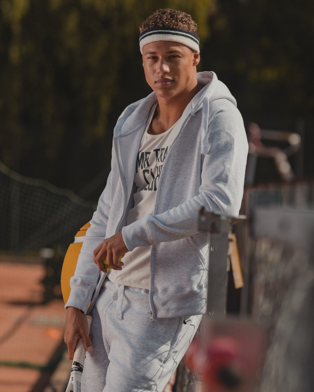 Person wearing a light grey ziphoodie on a tennis court outside