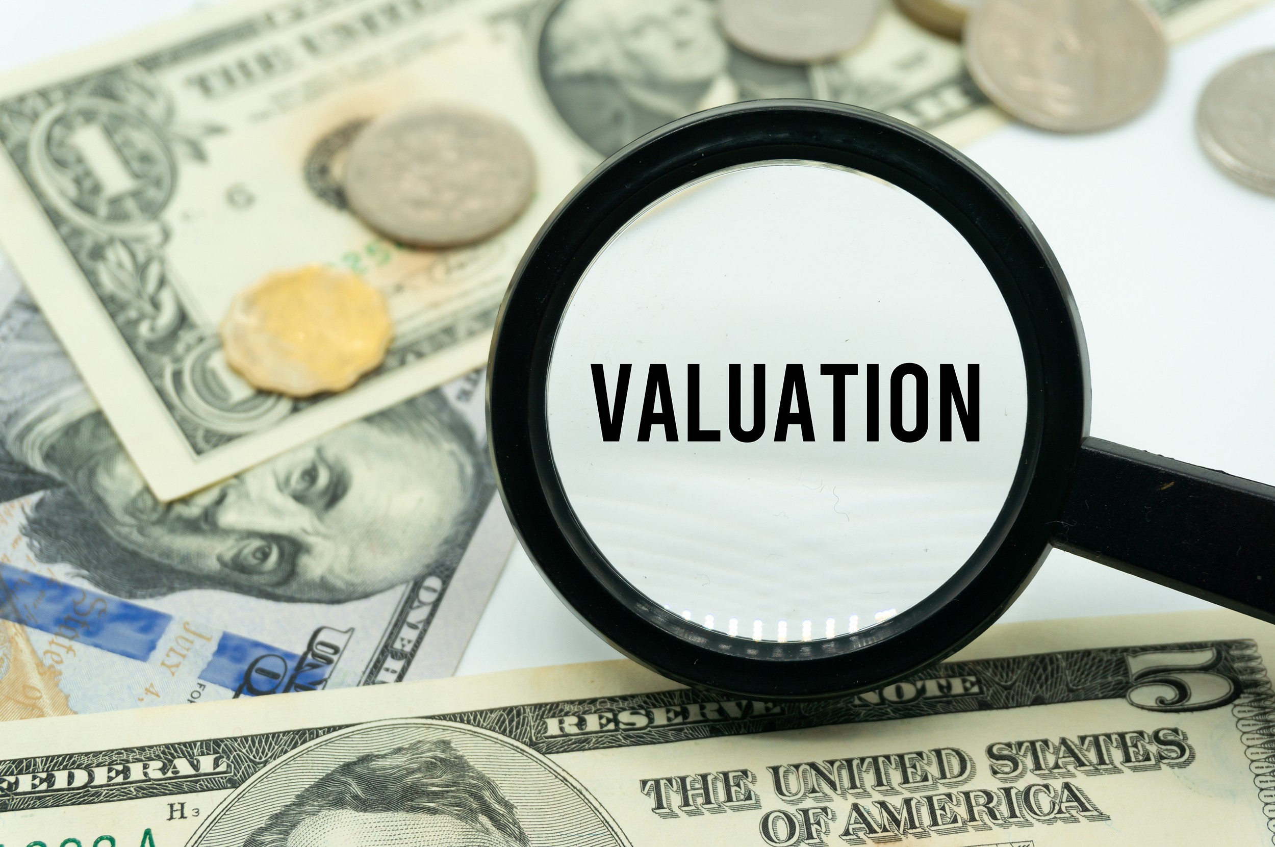 Valuation.Magnifying glass showing the words.Background of banknotes and coins.basic concepts of finance.Business theme.Financial terms.