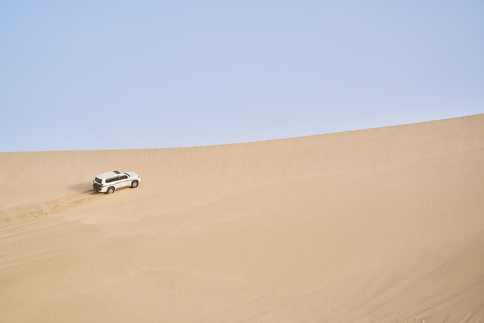 Un 4x4 blanc qui grimpe une grande dune du désert du Qatar sous un ciel bleu, là où la voiture doit tenir la chaleur