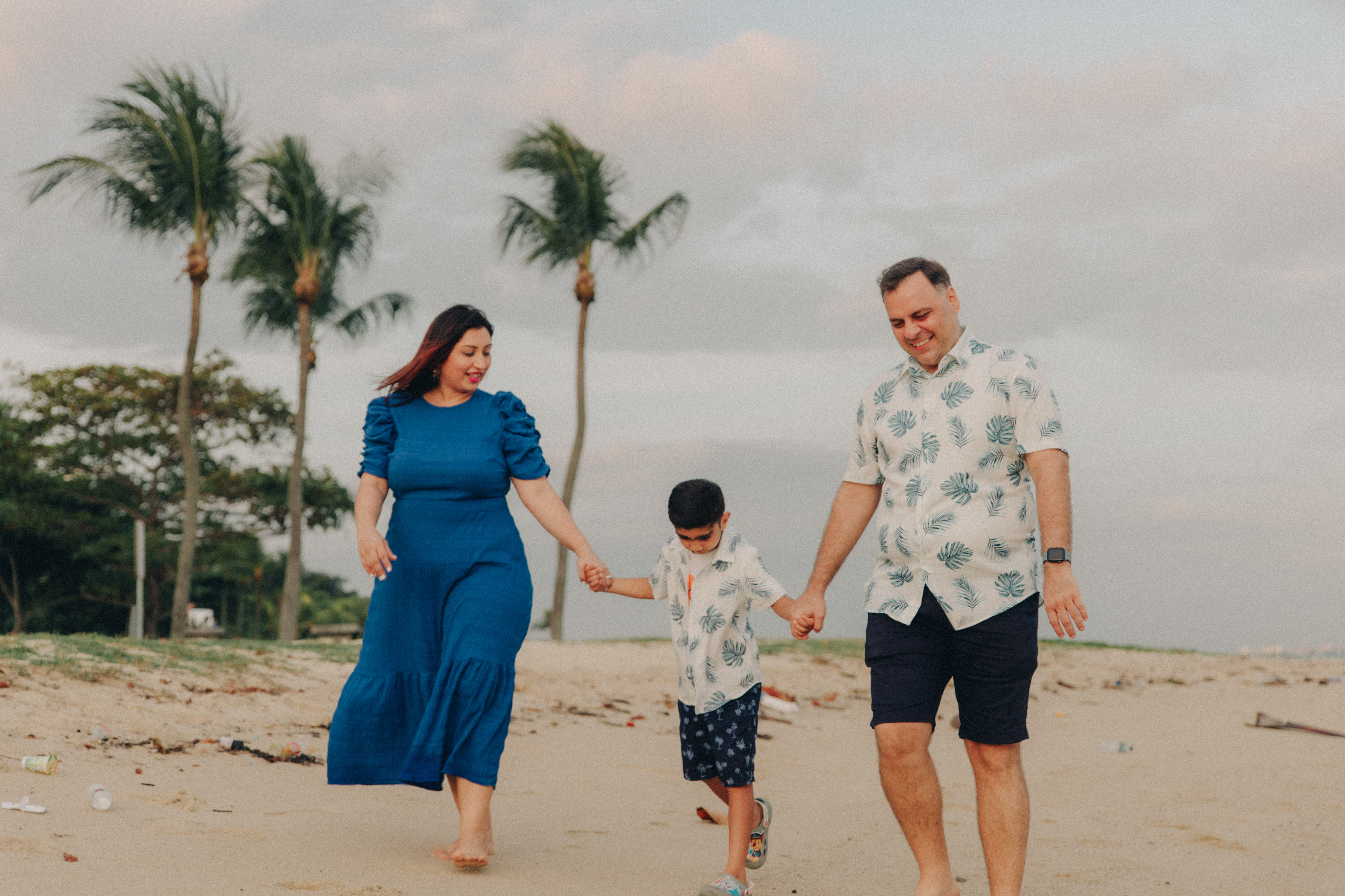 Candid moment of mother, father, and son walking along the beach in soft, neutral colored outfits.
