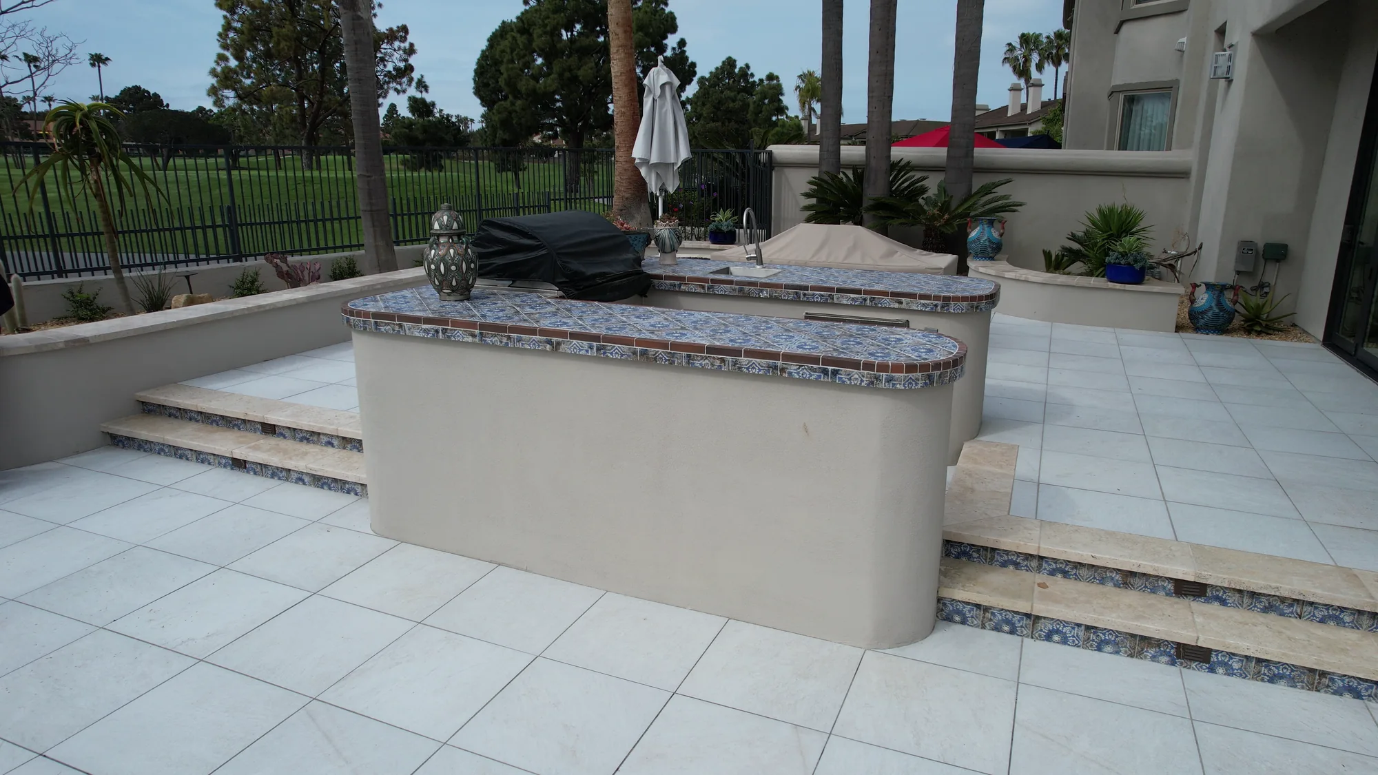 Outdoor counter with a tiled top on a pale paved patio beside the house.