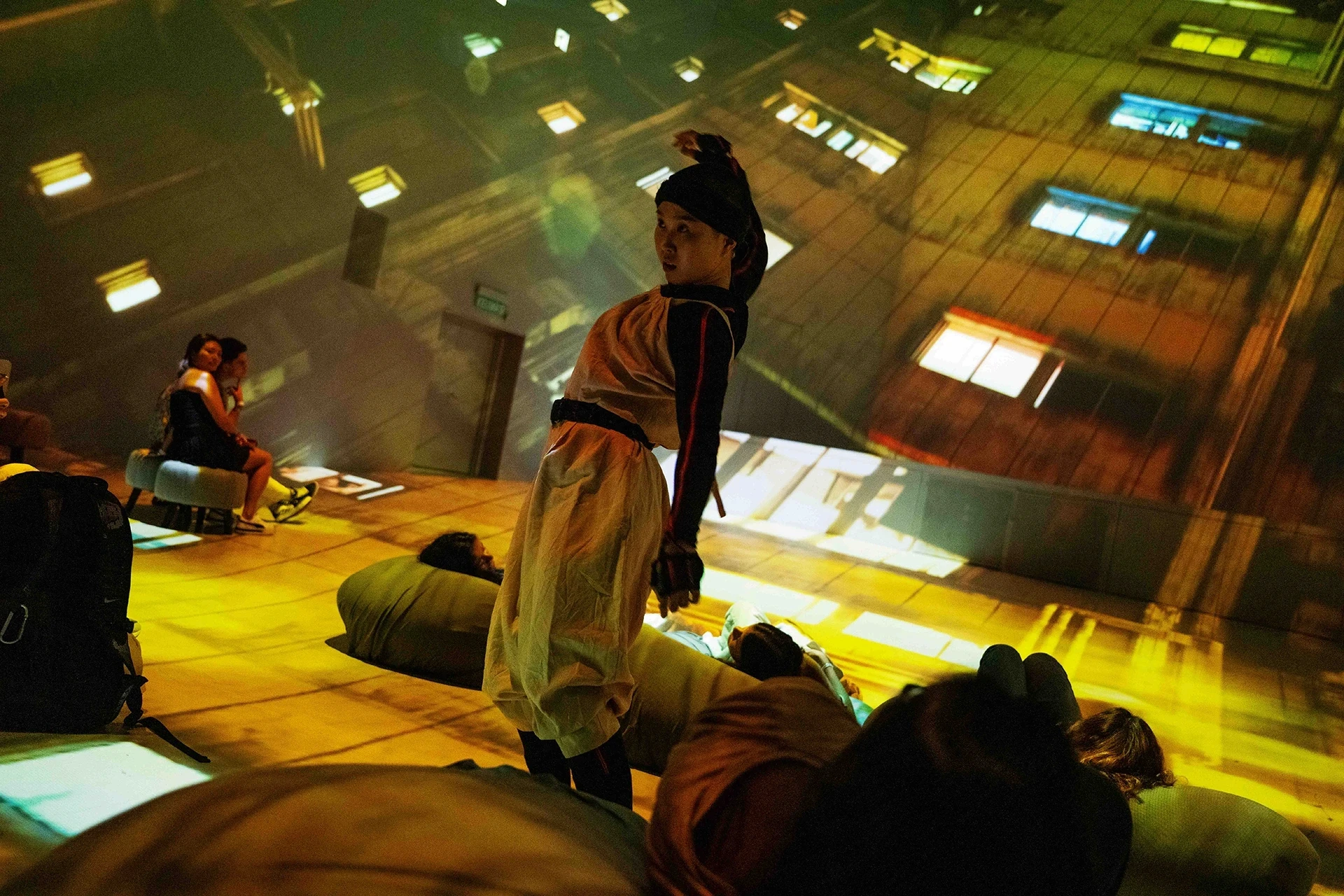 Performer surrounded by people on the floor, projected building lights.