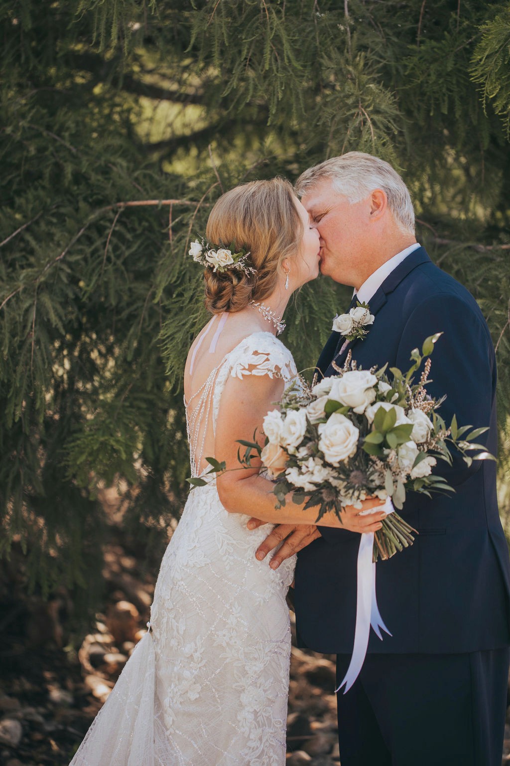 Bride and groom kissing with white rose bouquet at outdoor Iowa wedding.