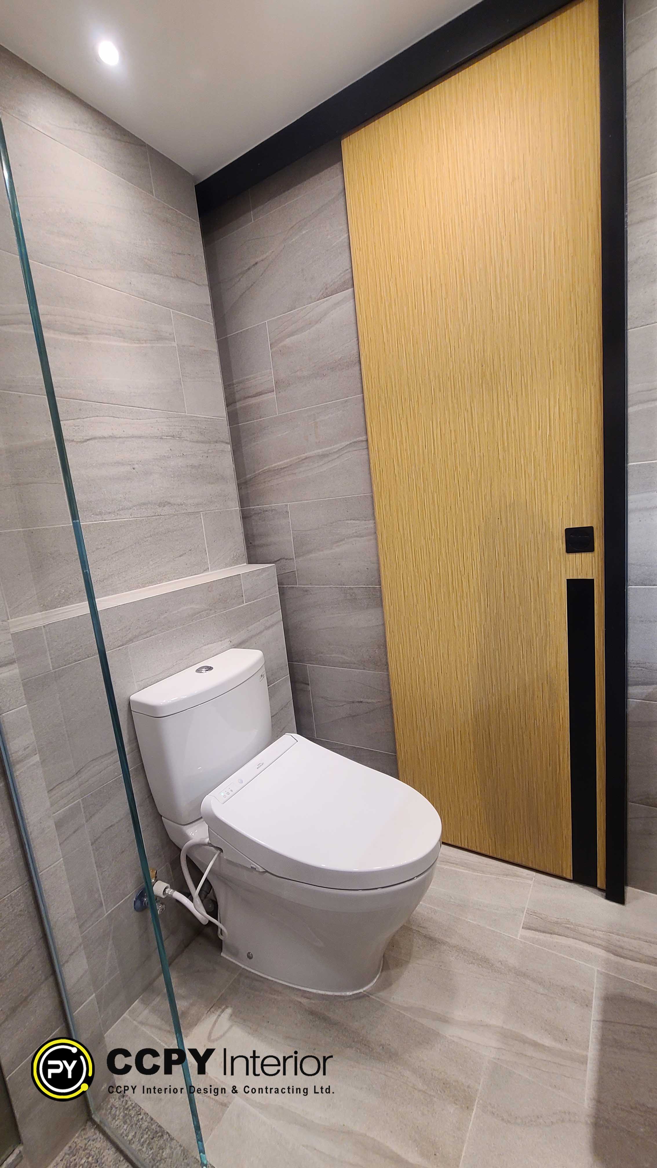 The selected region shows a modern bathroom featuring a white toilet, light gray stone-textured wall tiles, a glass shower partition, and a light wood-paneled door with black hardware.
