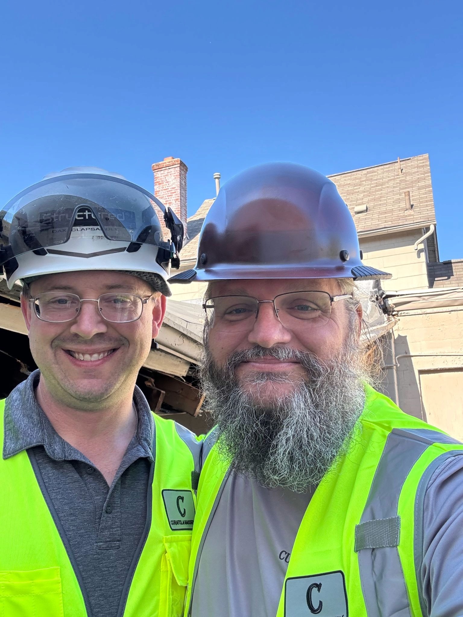 Two construction professionals wearing safety helmets and high-visibility vests at a restoration project.