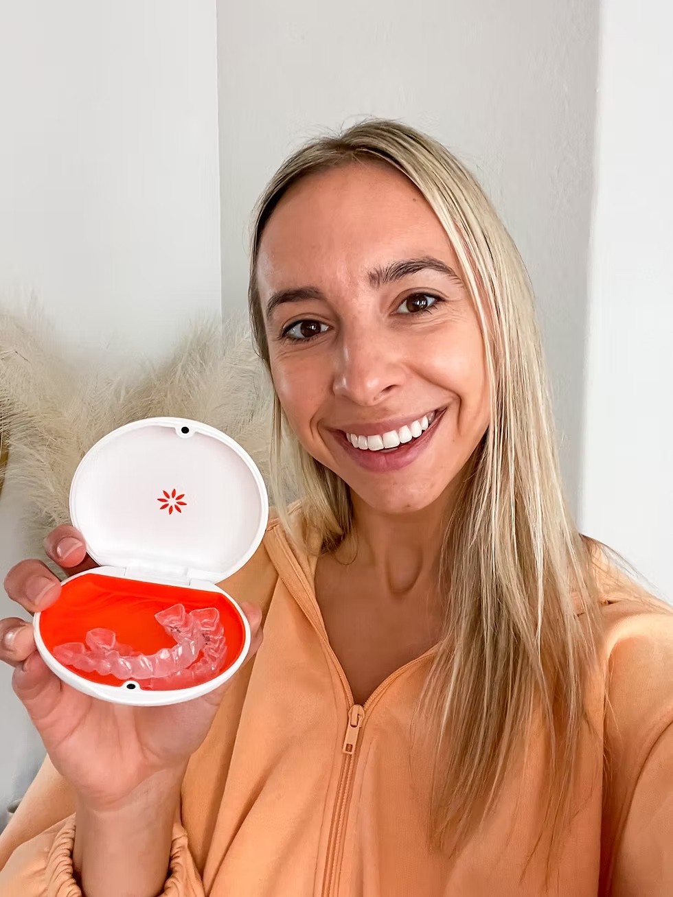 Invisalign treatment in Dubai with a client smiling and holding her new retainer after completing the plan at Invisalign Center.
