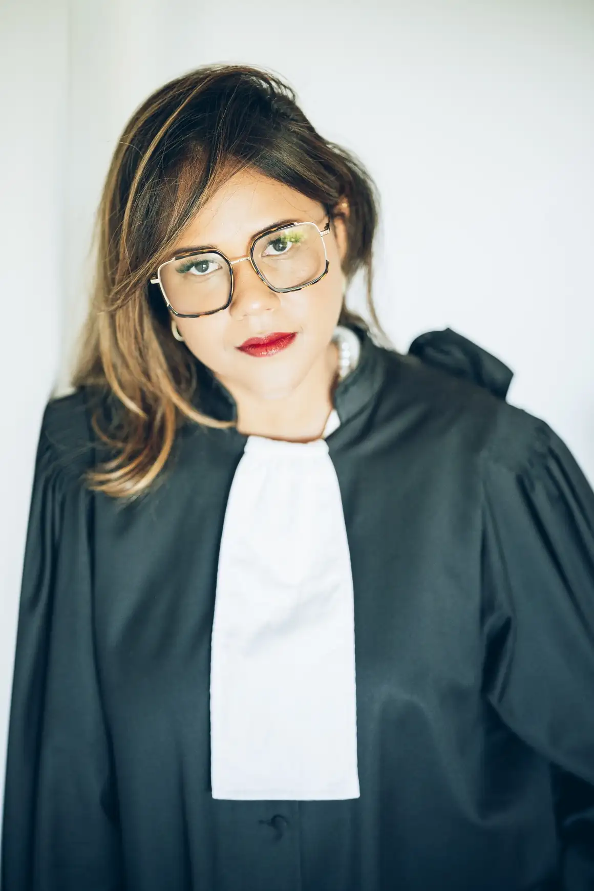 Portrait professionnel de Maître Julie Ramsamy portant sa robe d’audience et regardant l’objectif dans un environnement lumineux.