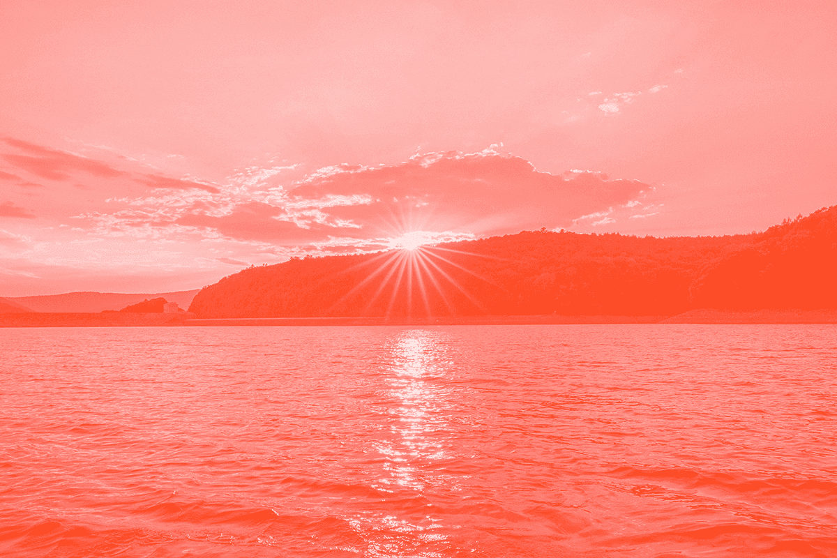 The sun rising over water with hills in the distance
