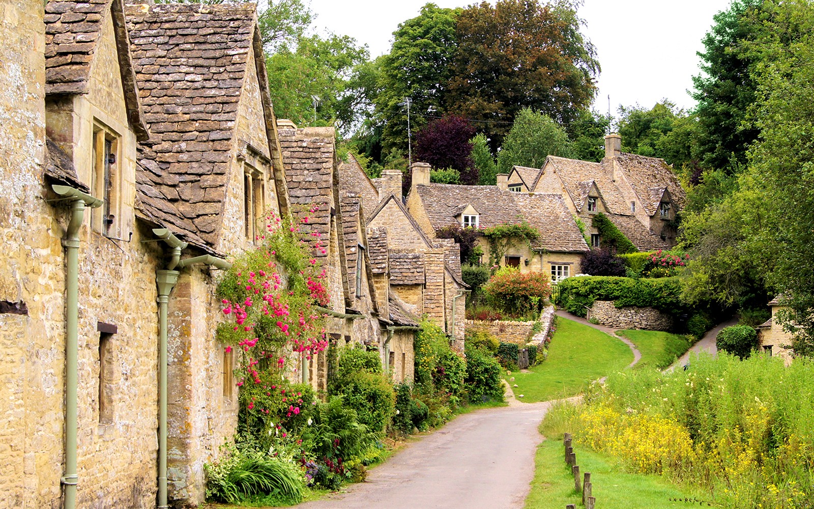 Arlington Row cottages in Bibury, Cotswolds, with stone walls and lush greenery.