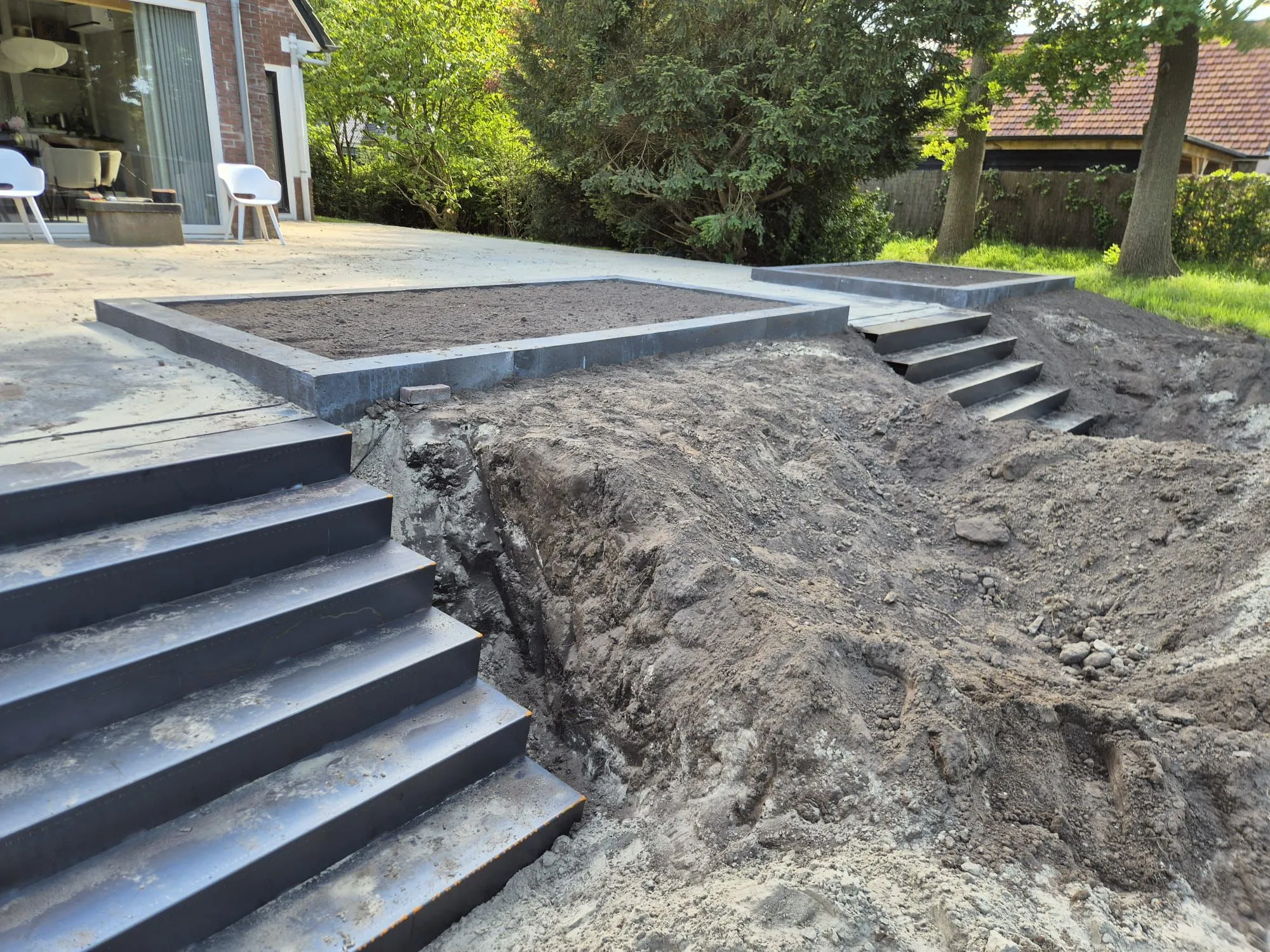Terras met oud-Hollandse tegels en gebakken klinkers, twee trappen naar lager gelegen tuin, grondwerk in uitvoering.