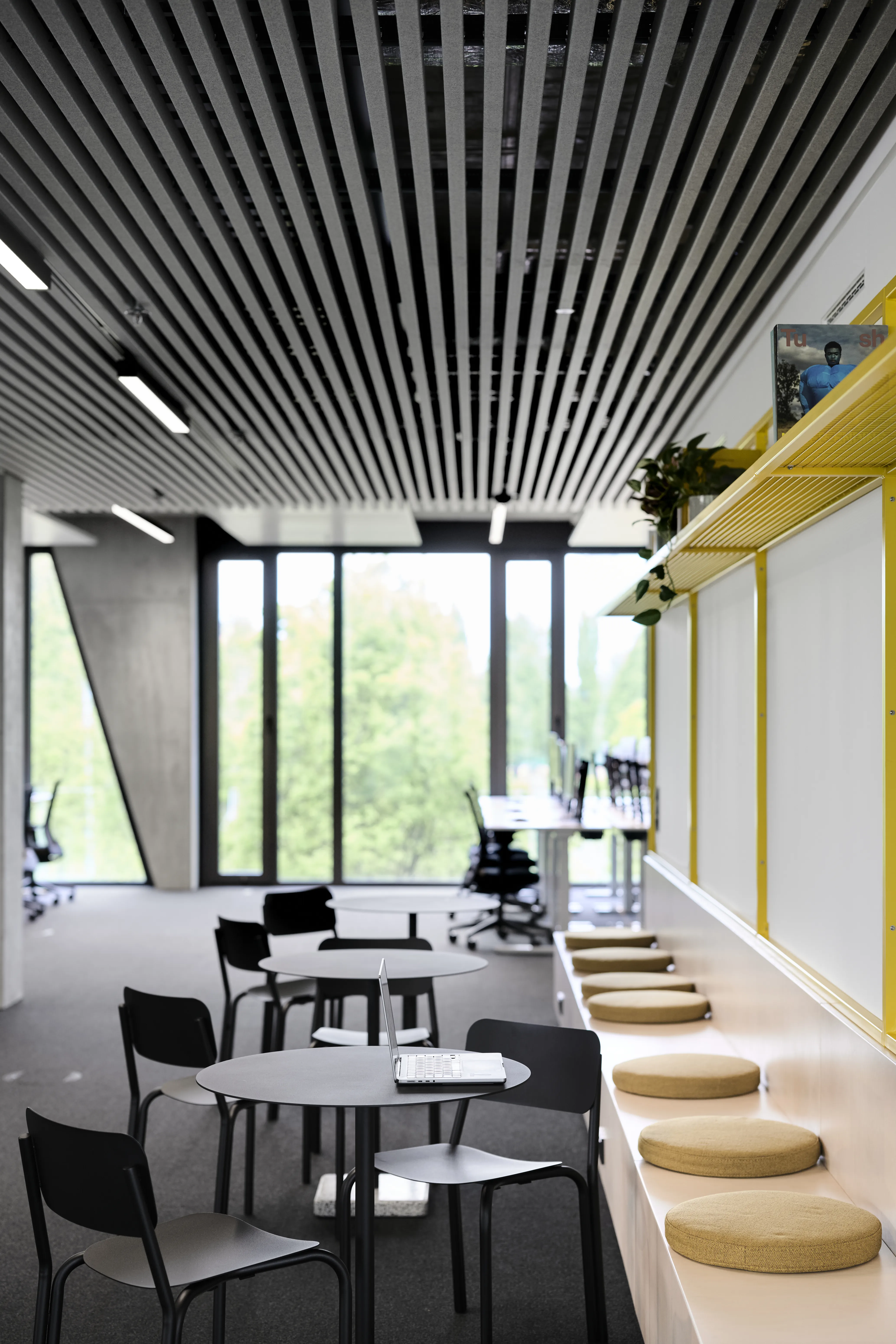 Café seating at ENPAL with round black tables and chairs next to a white sideboard with built-in bench and round seat cushions under a yellow mesh shelf.