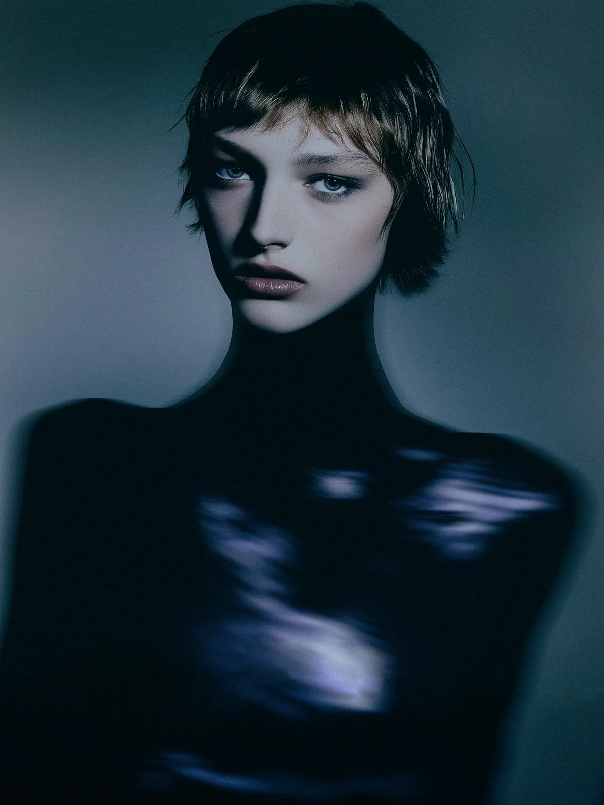 Fashion portrait with a short fringe and a dark glossy top in blue studio lighting.